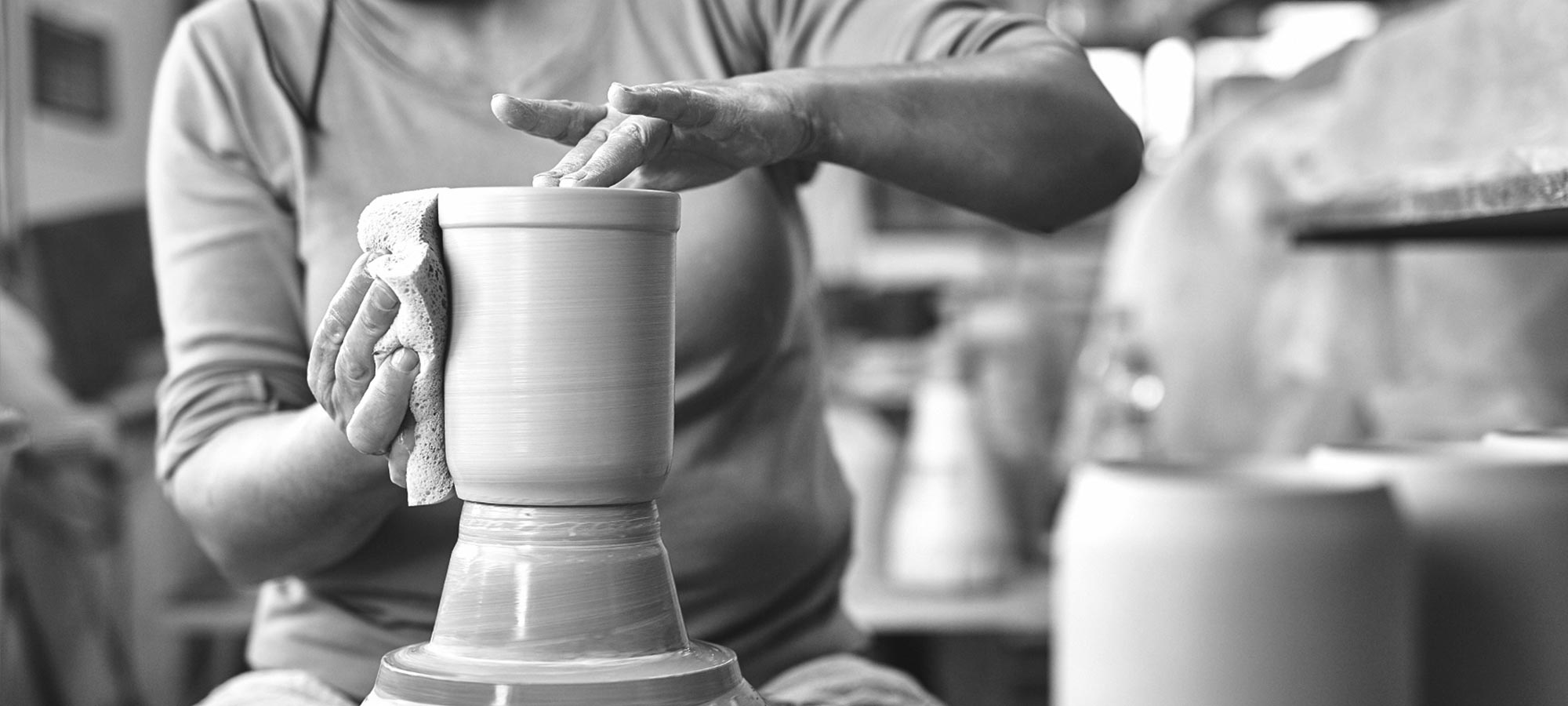 Hände formen einen personalisierten Bierkrug aus Ton auf einer Töpferscheibe, Details der Handwerkskunst sichtbar