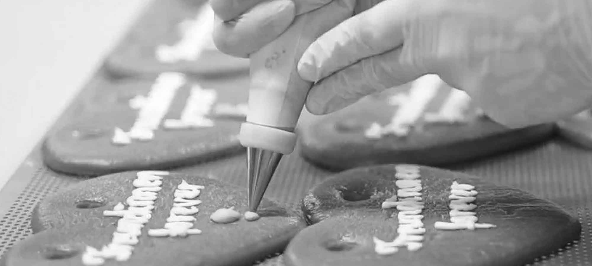 Hand in weißem Handschuh verziert personalisierte Lebkuchenherzen mit Zuckerguss für Oktoberfest-Geschenke, Detailansicht.