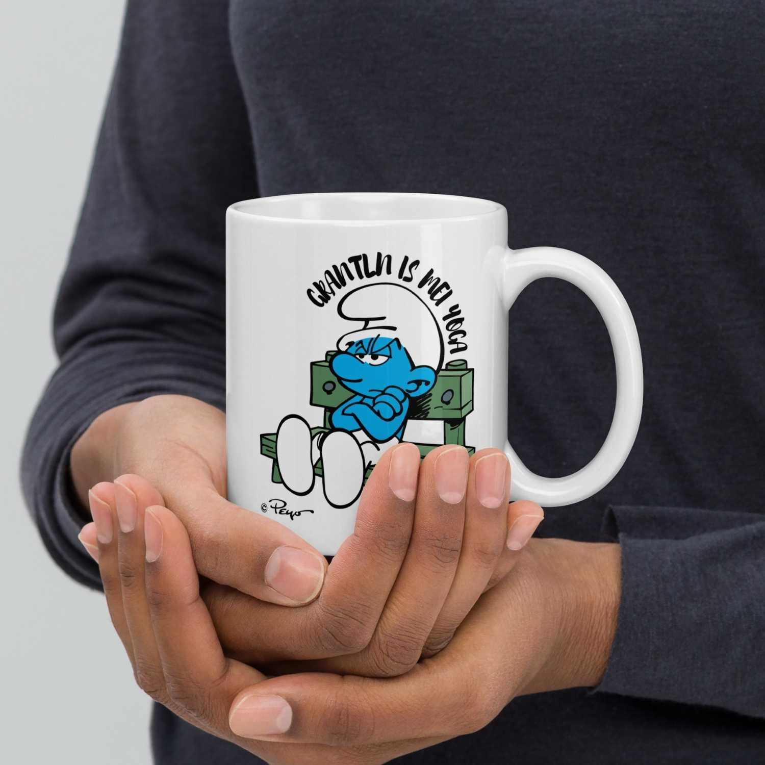 Weiße Porzellantasse mit blauer Schlumpffigur und Text „Grantln is mei Yoga“, Motiv gegenüber dem Henkel, 330 ml.
