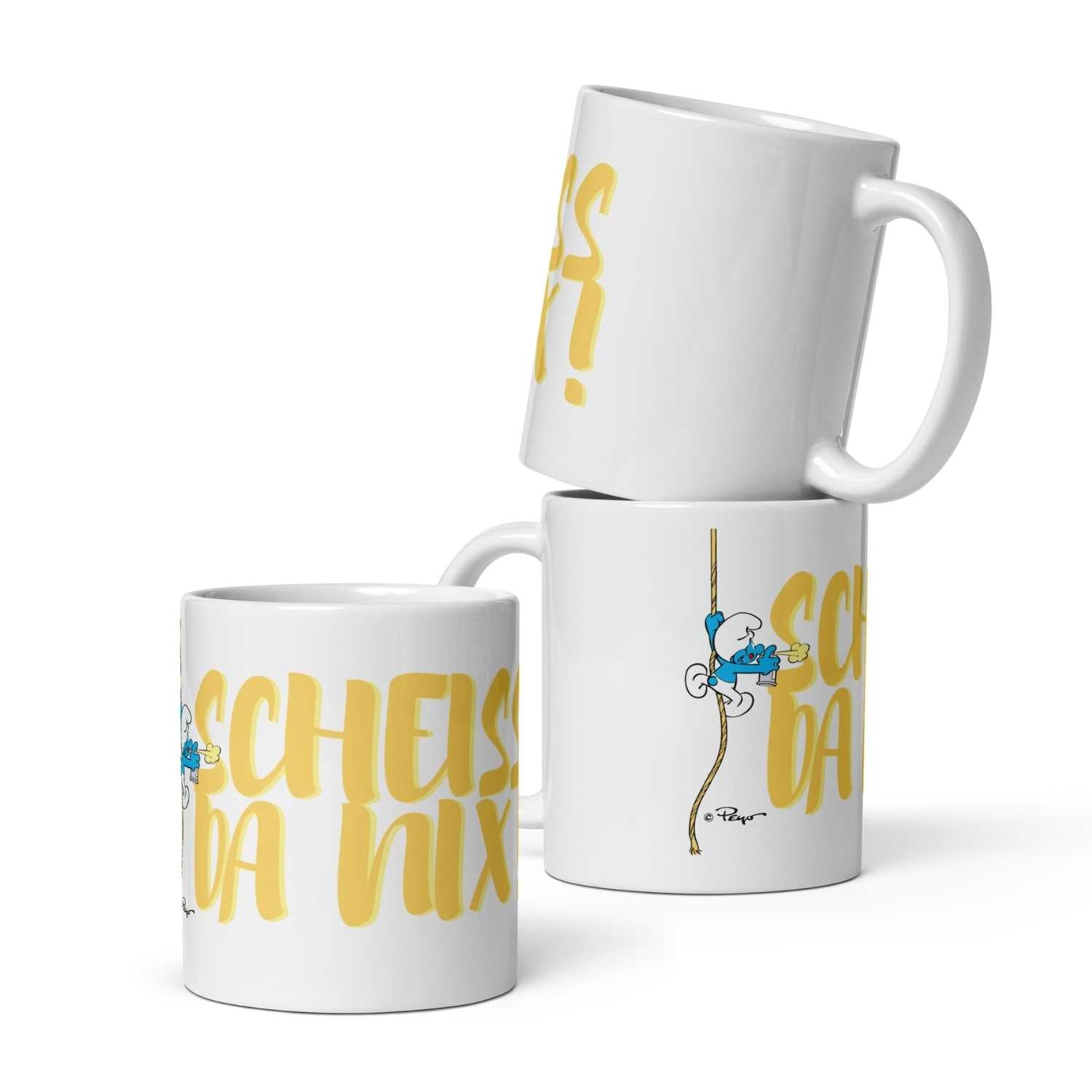 Weiße Porzellantasse mit Henkel, bedruckt mit Schlumpf-Motiv und dem Schriftzug „Scheiß da nix“, ca. 330 ml Füllmenge.