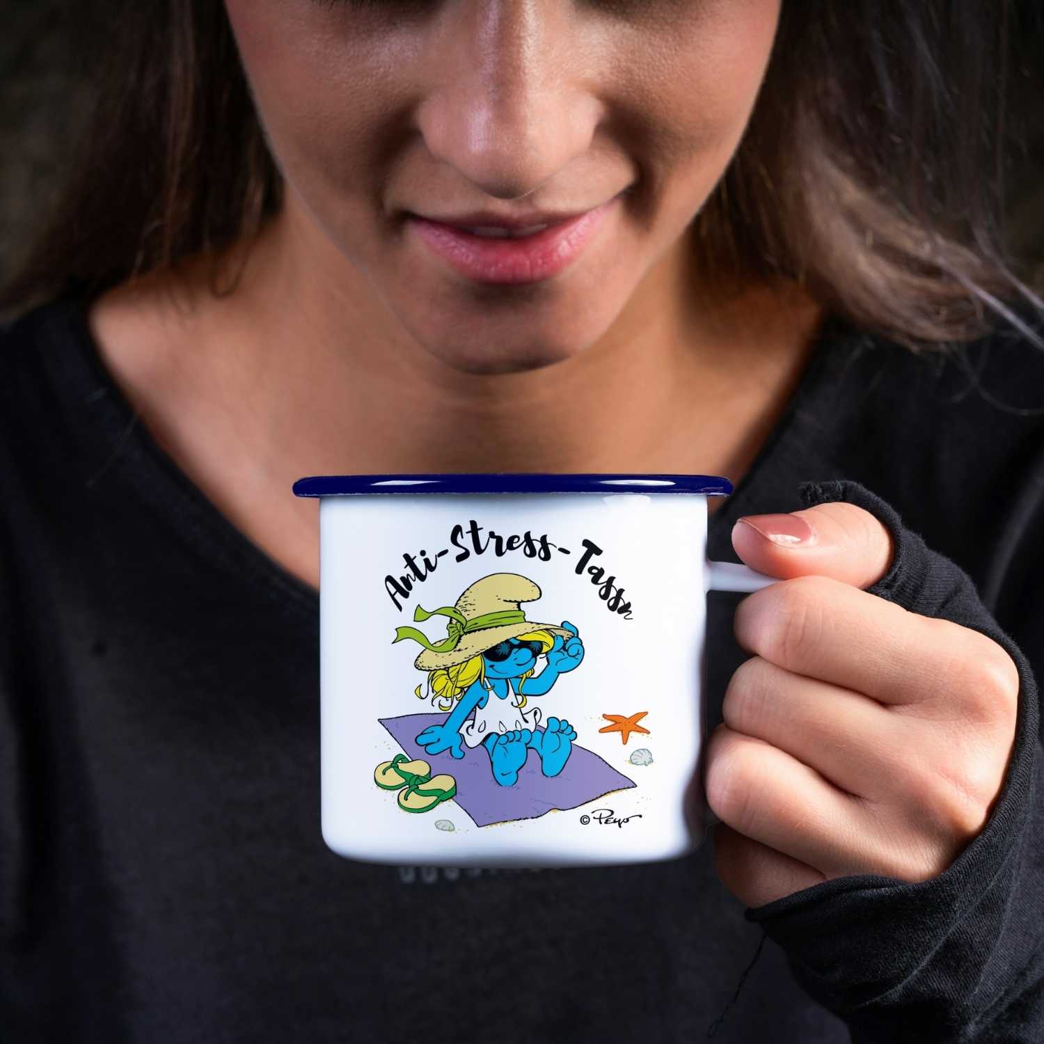 Weiße Emaille-Tasse mit blauem Rand und Aufdruck „Anti Stress-Tass’n“ sowie Schlumpf-Motiv; Füllmenge ca. 330 ml.