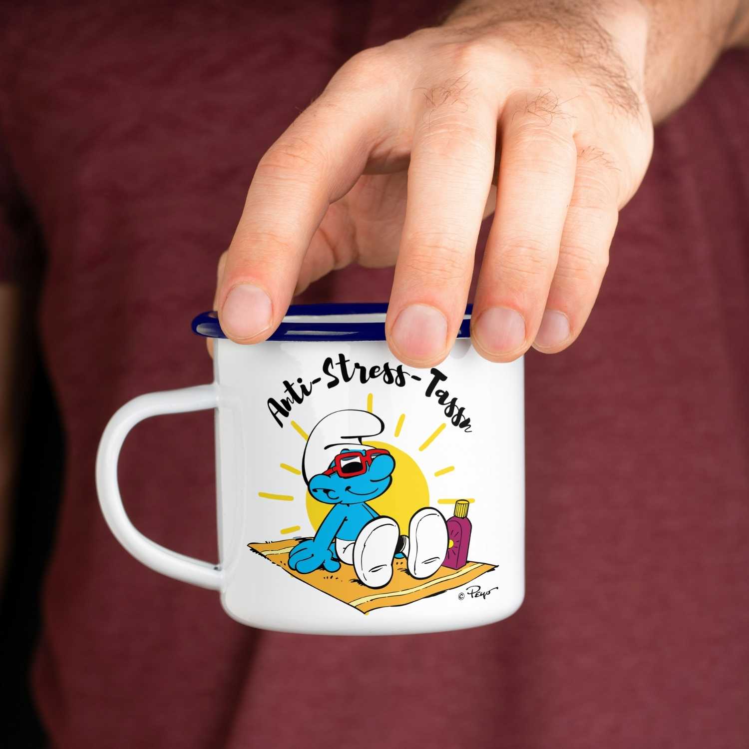 Emailletasse mit Schlumpf-Motiv und Aufschrift „Anti Stress Tass'n“, blauer Rand, weiße Oberfläche, ca. 330 ml.