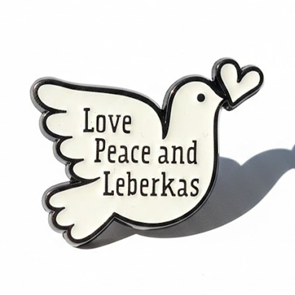 Schwarz-weißer Emaille-Pin in Taubenform mit Aufschrift Love, Peace and Leberkas, Herz im Schnabel.
