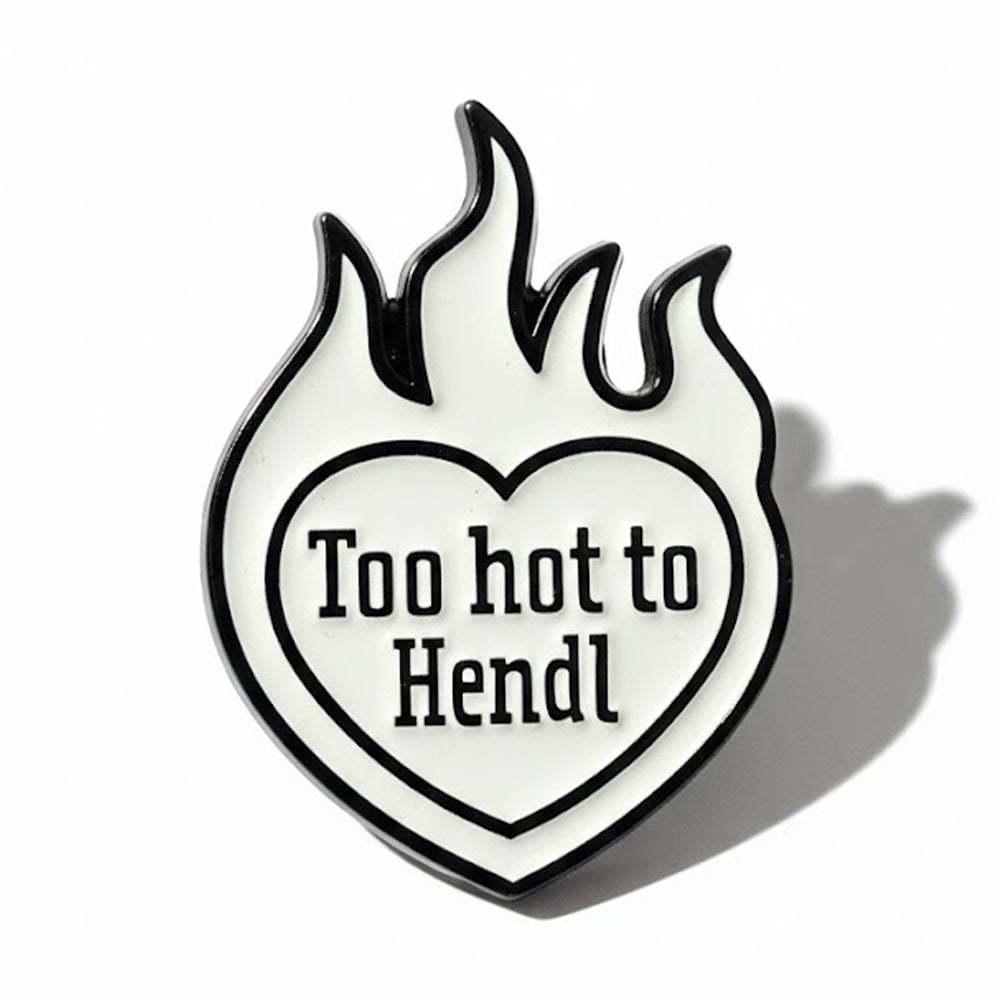 Schwarz-weißer Emaille-Pin in Flammenform mit Herz und Aufschrift "Too hot to Hendl". Lustiger Anstecker.