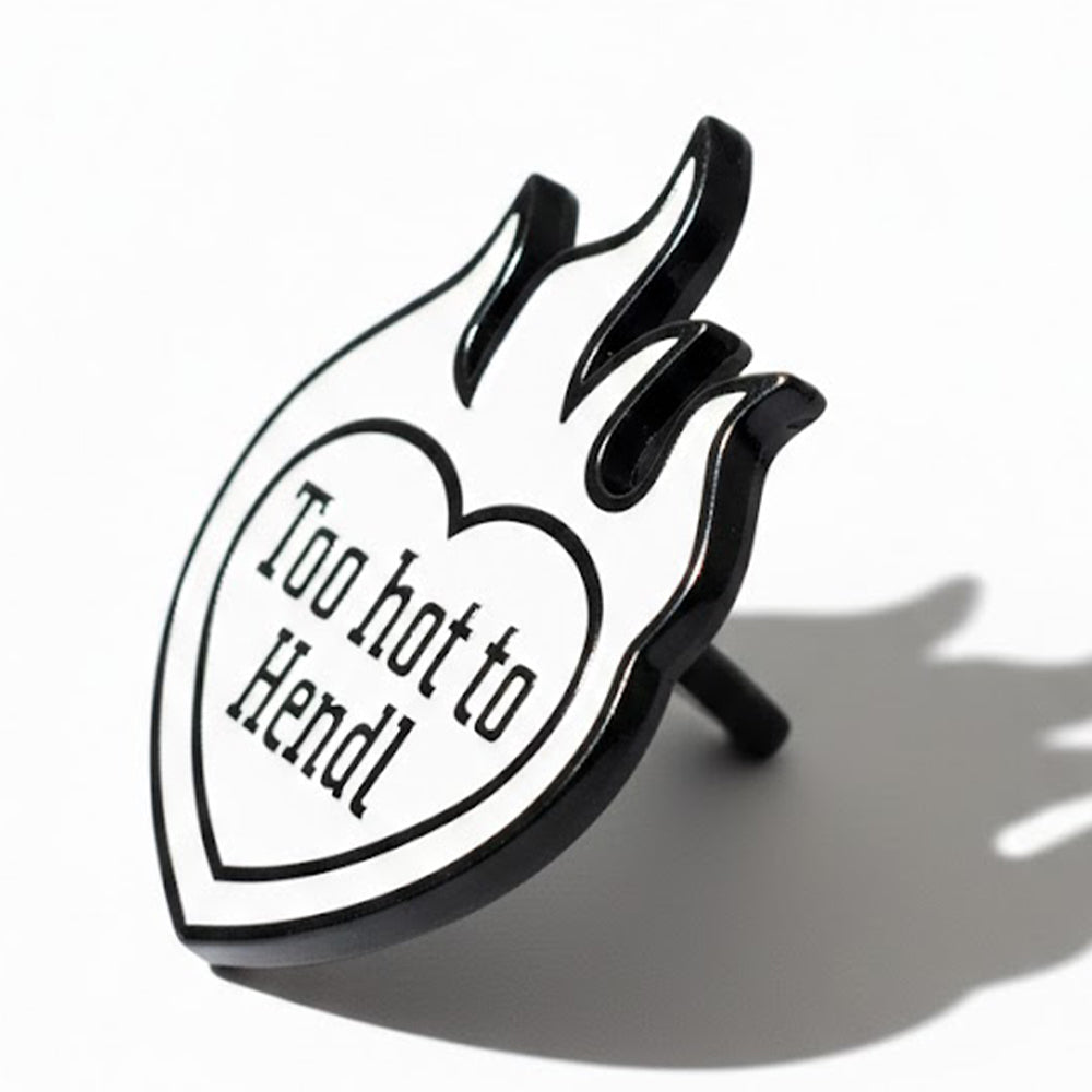 Schwarz-weißer Emaille Pin in Flammenform mit Herzmotiv und lustigem "Too hot to Hendl" Spruch.