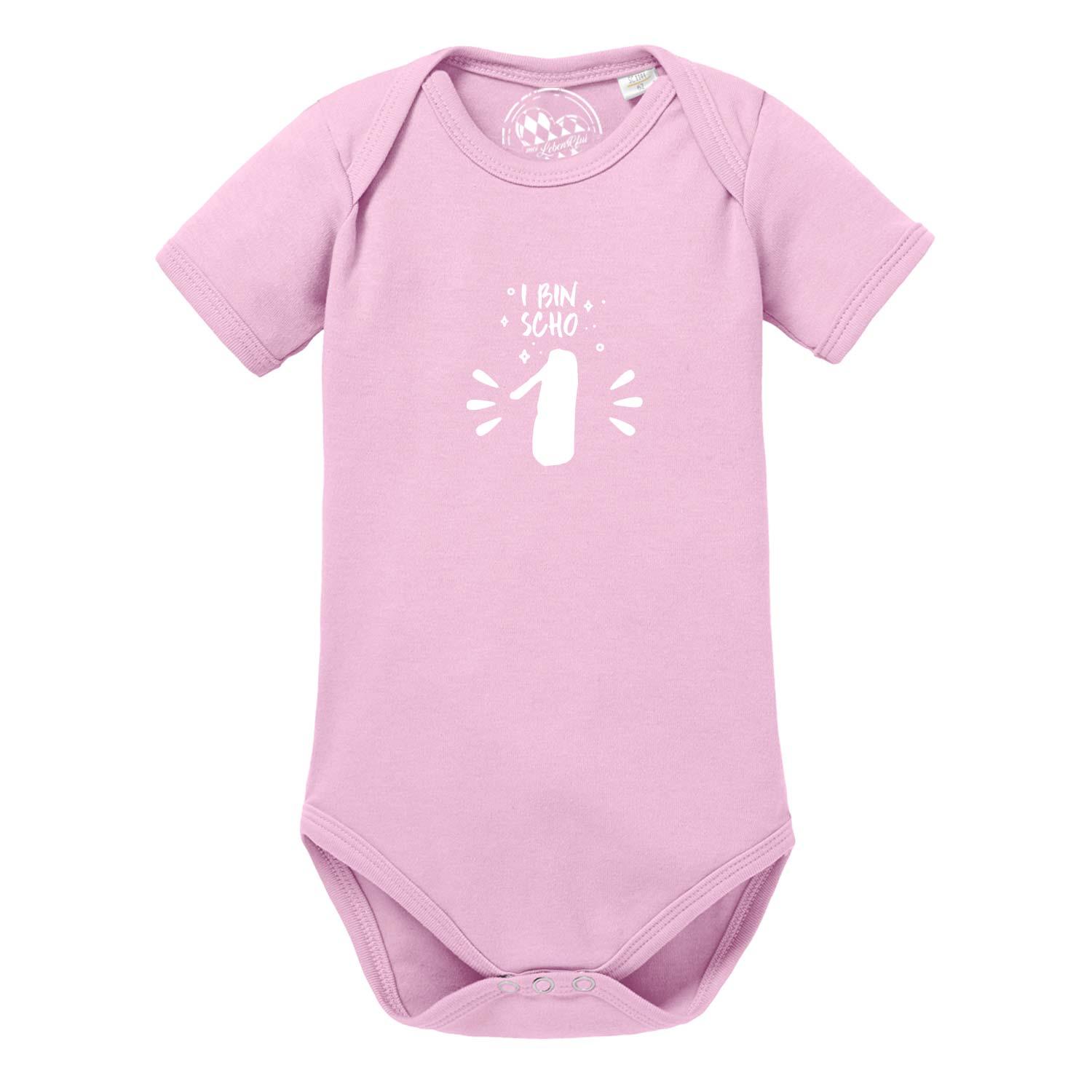 Rosa Baby Body "I bin scho 1!" mit weißem Aufdruck zum ersten Geburtstag, kurzärmlig aus Baumwolle.
