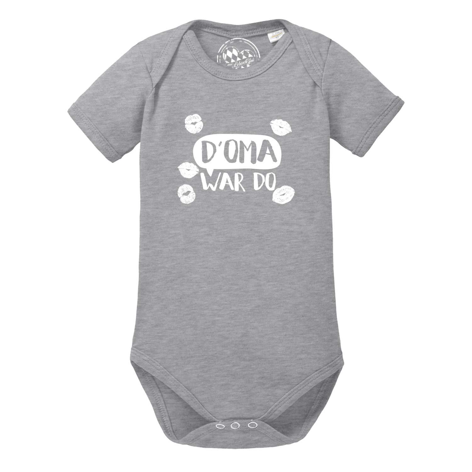 Weißer Babybody mit kurzen Ärmeln, schwarzem Schriftzug „D’ Oma war do…“ und kleinem Herzmotiv vorn; aus Baumwolle.