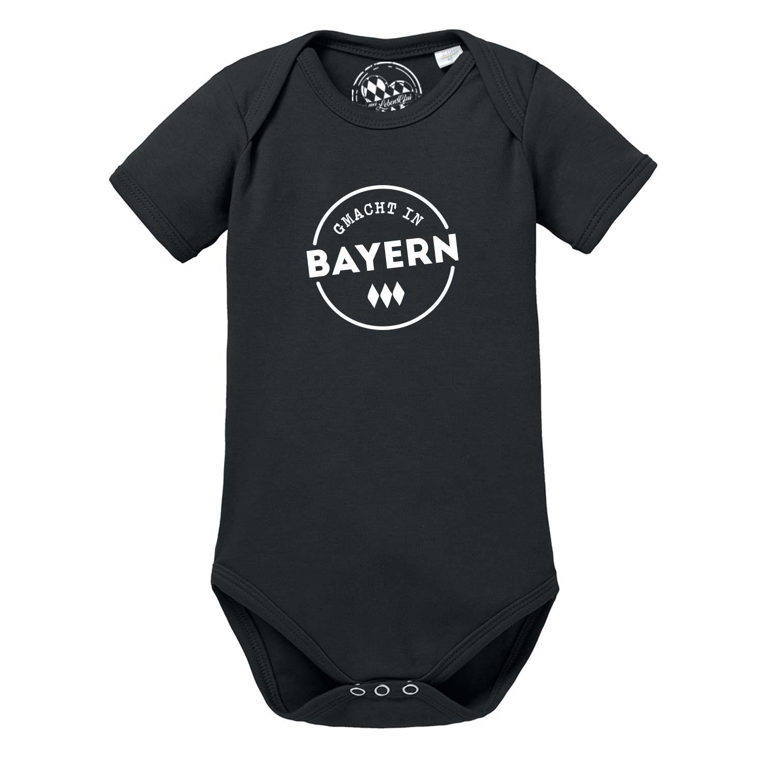 Kurzärmeliger weißer Babybody mit blauem Bayern-Rautenherz und rotem Schriftzug „Gmacht in Bayern“, aus Baumwolle.