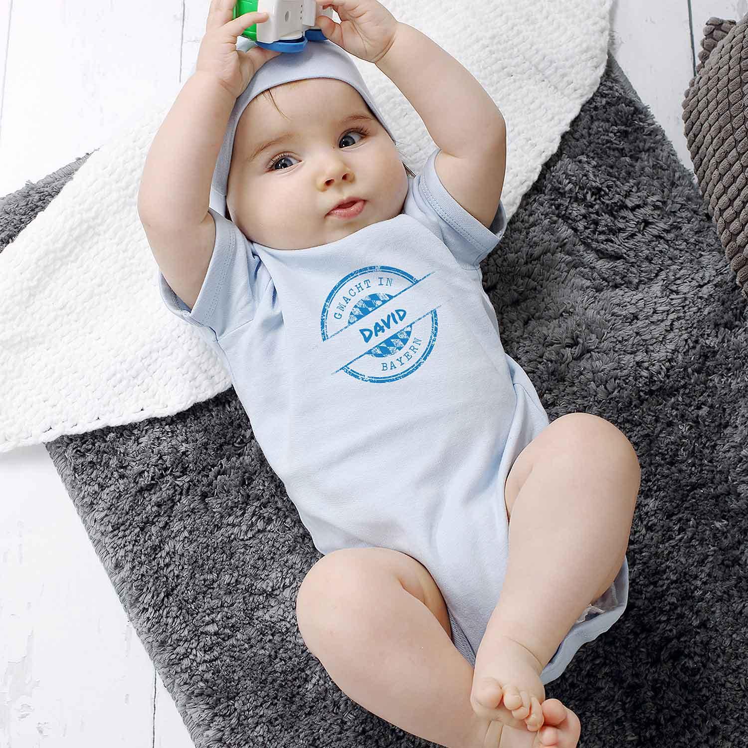 Blauer Baby-Body mit weißem Aufdruck „gmacht in Bayern“ und personalisierbarem Wunschnamen, Kurzarm, Baumwolle.