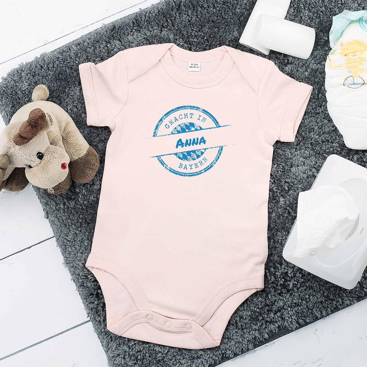 Rosa Baby-Body mit bayrischem Schriftzug „gmacht in Bayern“ und individuellem Wunschnamen, Druckknöpfe im Schritt, Baumwolle.