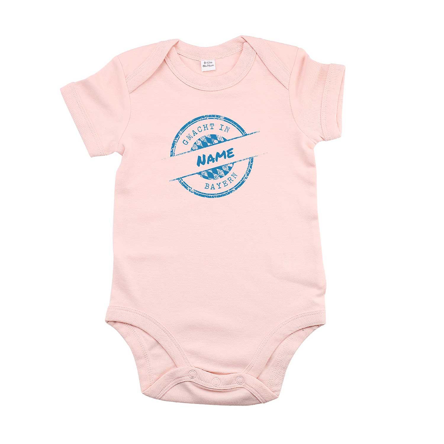 Rosa Baby-Body mit weißem Schriftzug „gmacht in Bayern“ und personalisierbarem Wunschnamen auf der Brust; kurze Ärmel, drei Druckknöpfe im Schritt, aus Baumwolle.