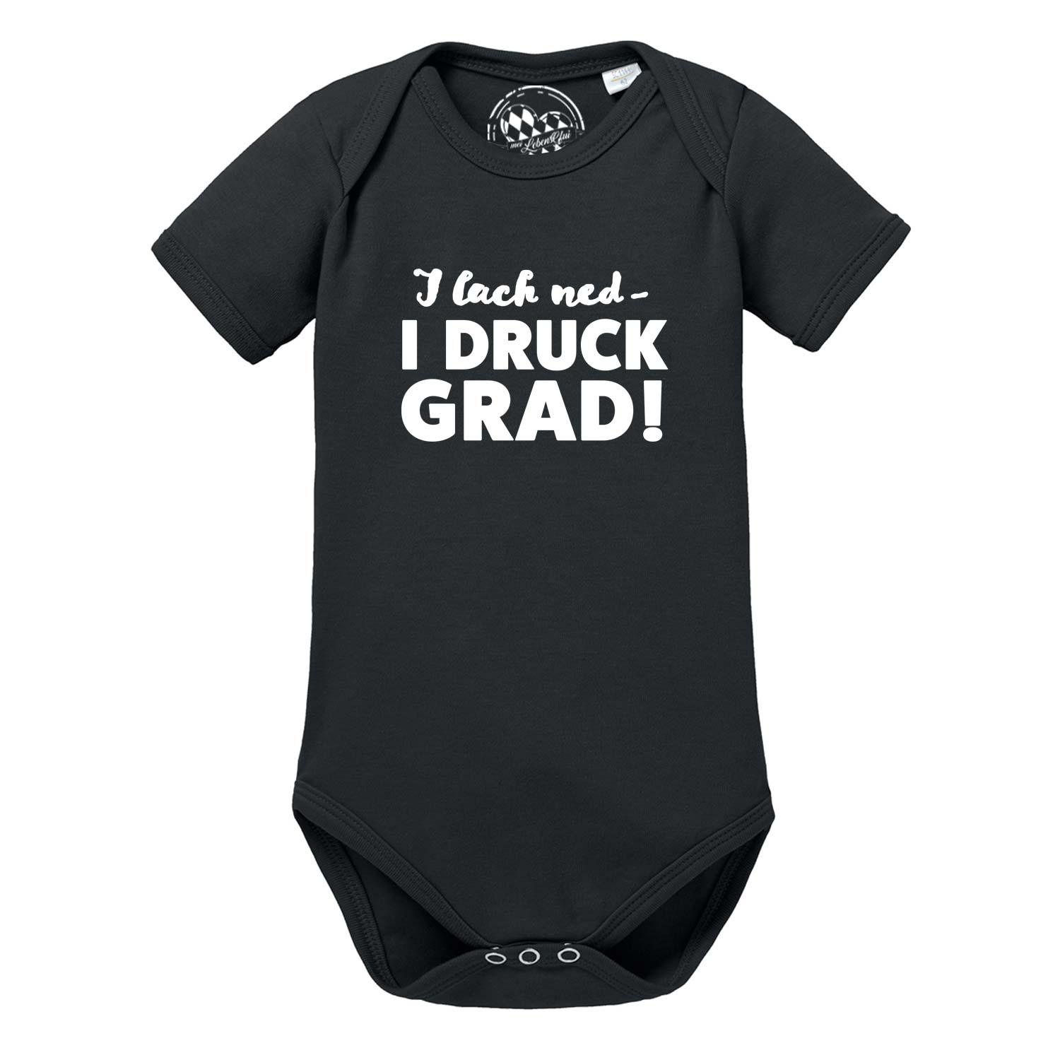 Weißer Baby-Body mit bayerischem Schriftzug „I lach ned…“, runder Halsausschnitt, kurze Ärmel, aus Baumwolle.