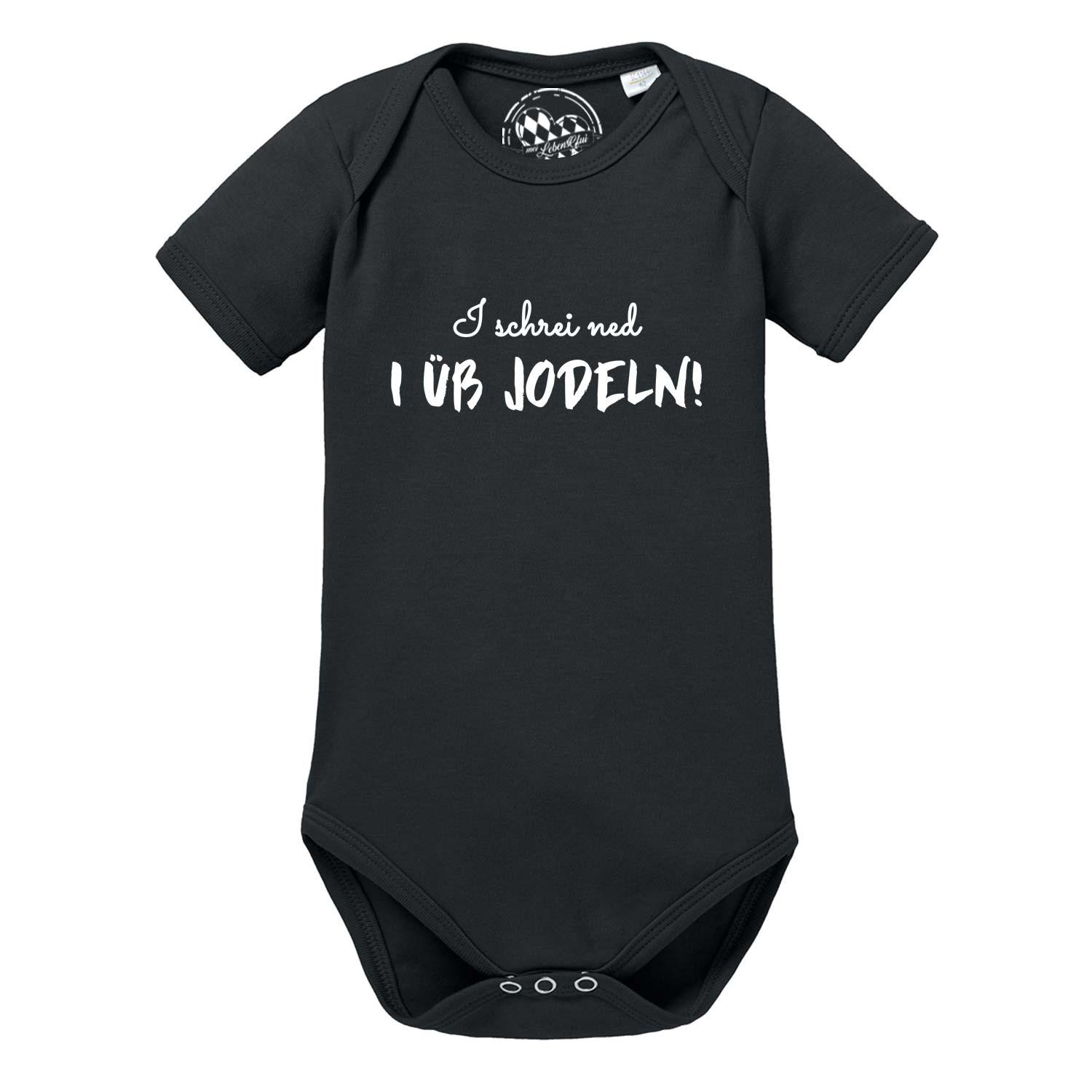 Weißer Kurzarm-Babybody mit schwarzem Aufdruck „I üb jodeln“ und Edelweiß-Motiv, aus weicher Baumwolle.