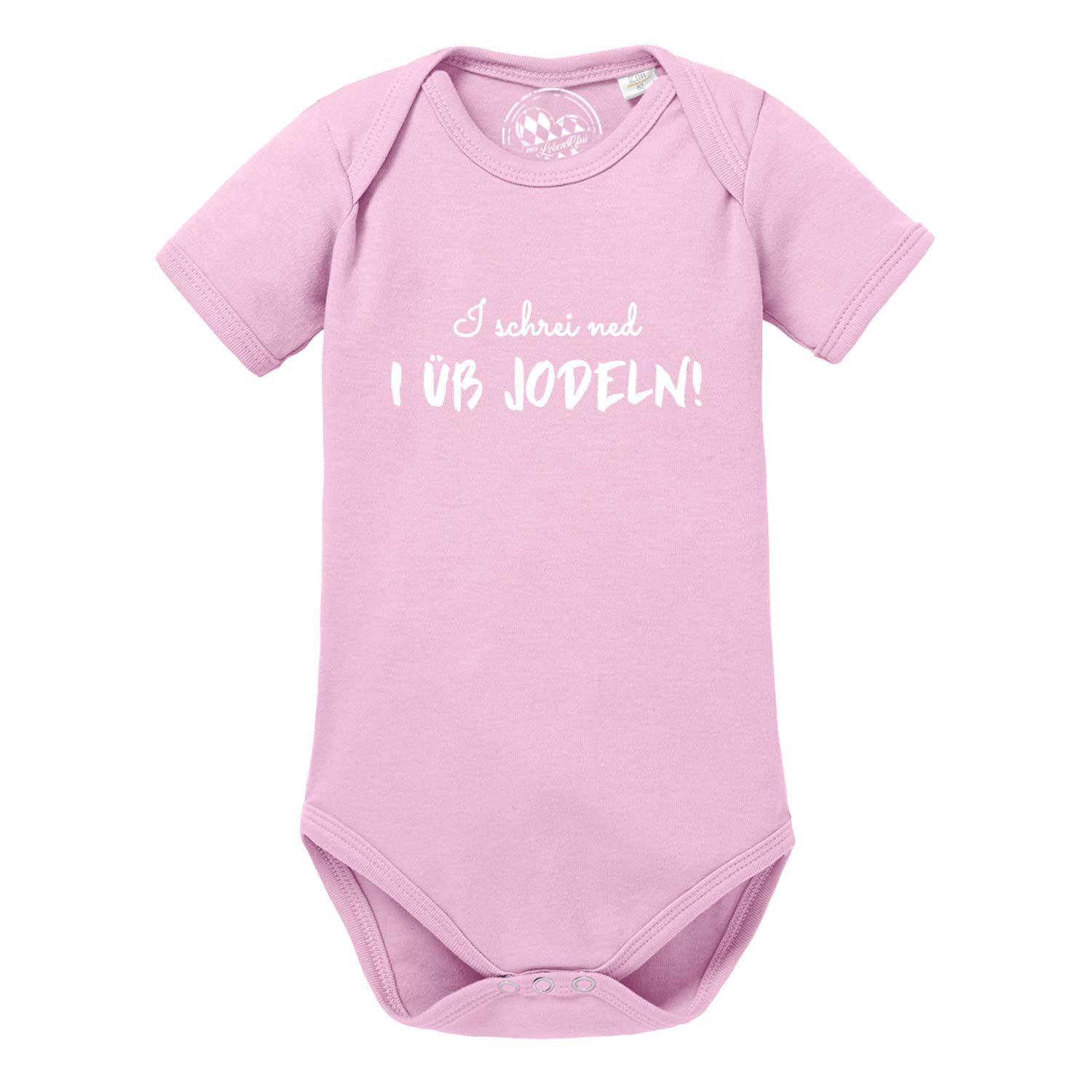 Weißer Babybody mit kurzen Ärmeln, blauem Herz-Motiv und Aufdruck „I üb jodeln“ auf der Brust; aus Baumwolle.