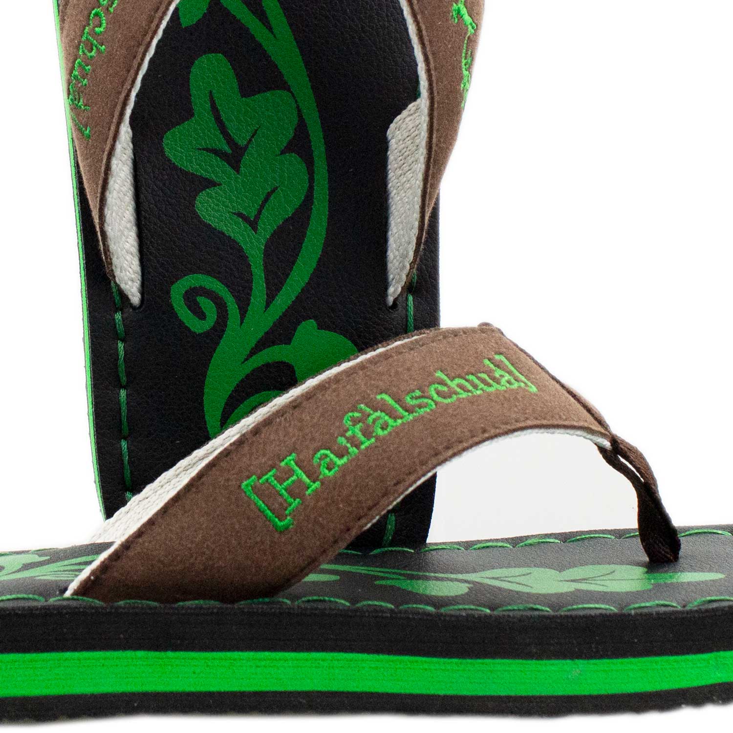 Badesandale Haferlschuh mit braunem Riemen, grünem Haferlschuh-Schriftzug und Blätter-Print auf schwarzem Fußbett.