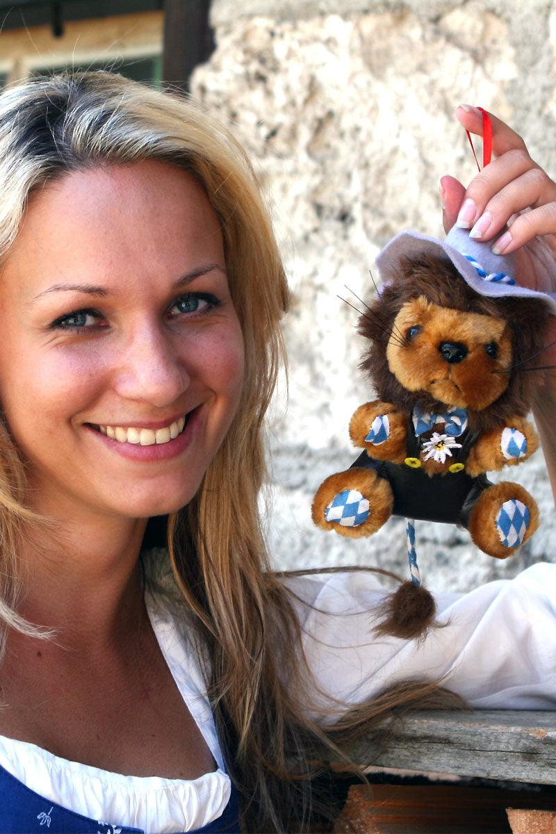 Plüschlöwe mit brauner Mähne, trägt grauen Filzhut und braune Lederhose im bayerischen Design aus weichem Stoff.