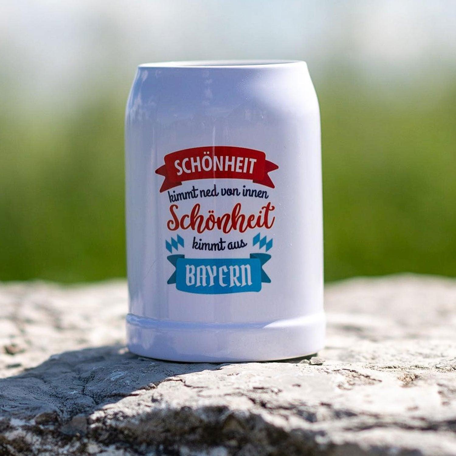 Weißer Bierkrug Schönheit kimmt aus... mit Wunschort und bayerischem Spruch auf Stein liegend