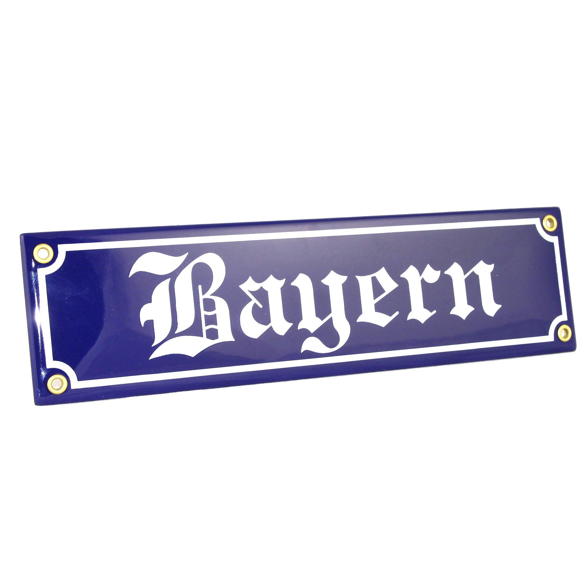Rechteckiges Emaille-Schild im Stil eines bayerischen Straßenschilds mit blau-weißem Rand und weißer Schrift auf Blau.