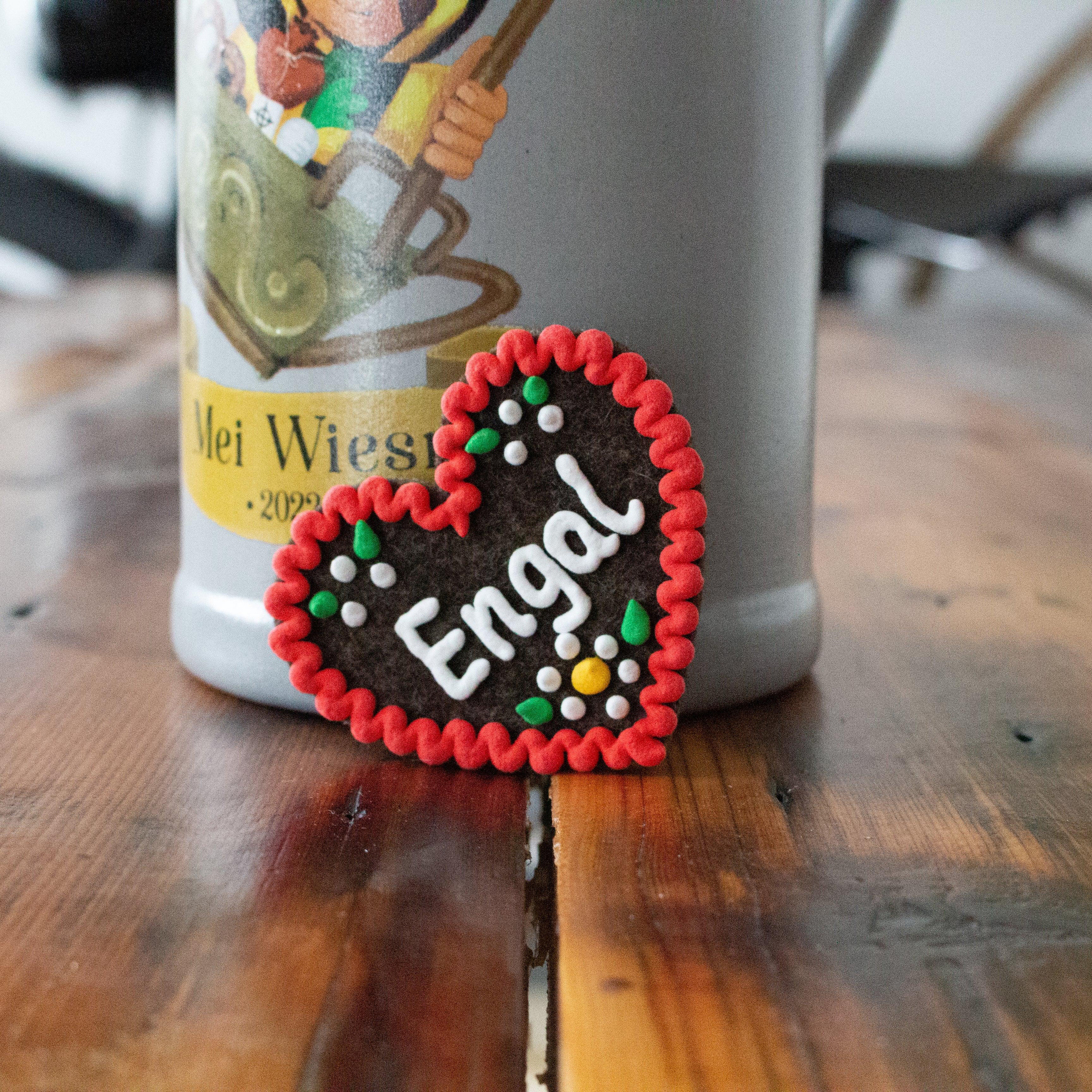 Herzförmiger Anstecker aus Filz mit gesticktem Schriftzug „Engal“ und Sicherheitsverschluss auf der Rückseite; ca. 6,5 x 7 cm, 3 mm dick.