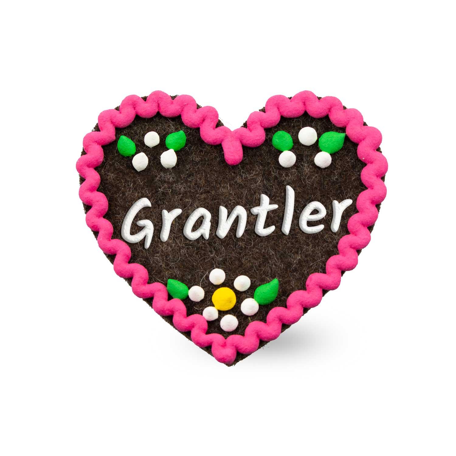 Herzförmiger Filzanstecker mit aufgesticktem Schriftzug „Grantler“ in Weiß, mit Sicherheitsverschluss auf der Rückseite, ca. 6,5 x 7 cm groß.