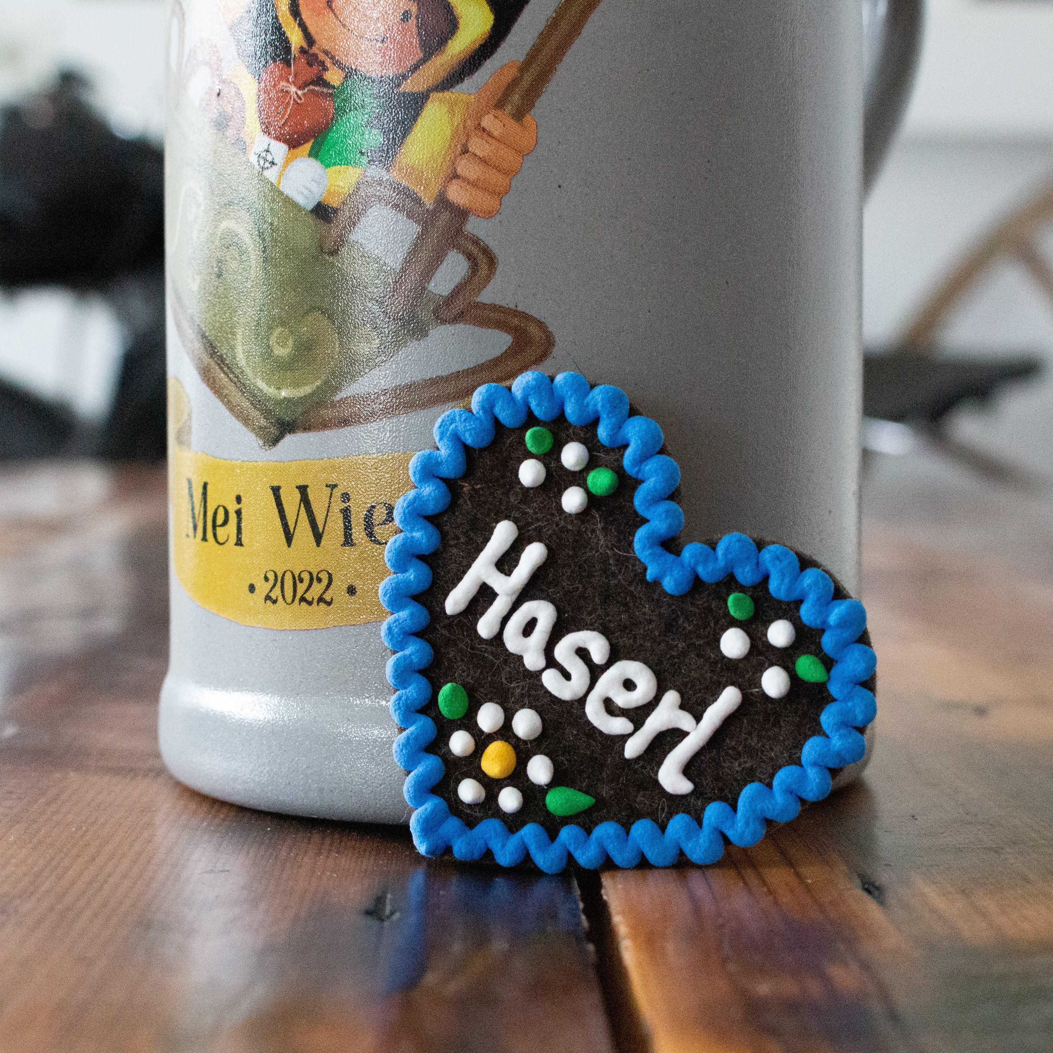 Herzförmiger Filz-Anstecker mit aufgesticktem Schriftzug „Haserl“ und Sicherheitsverschluss auf der Rückseite; Maße ca. 6,5 x 7 cm.