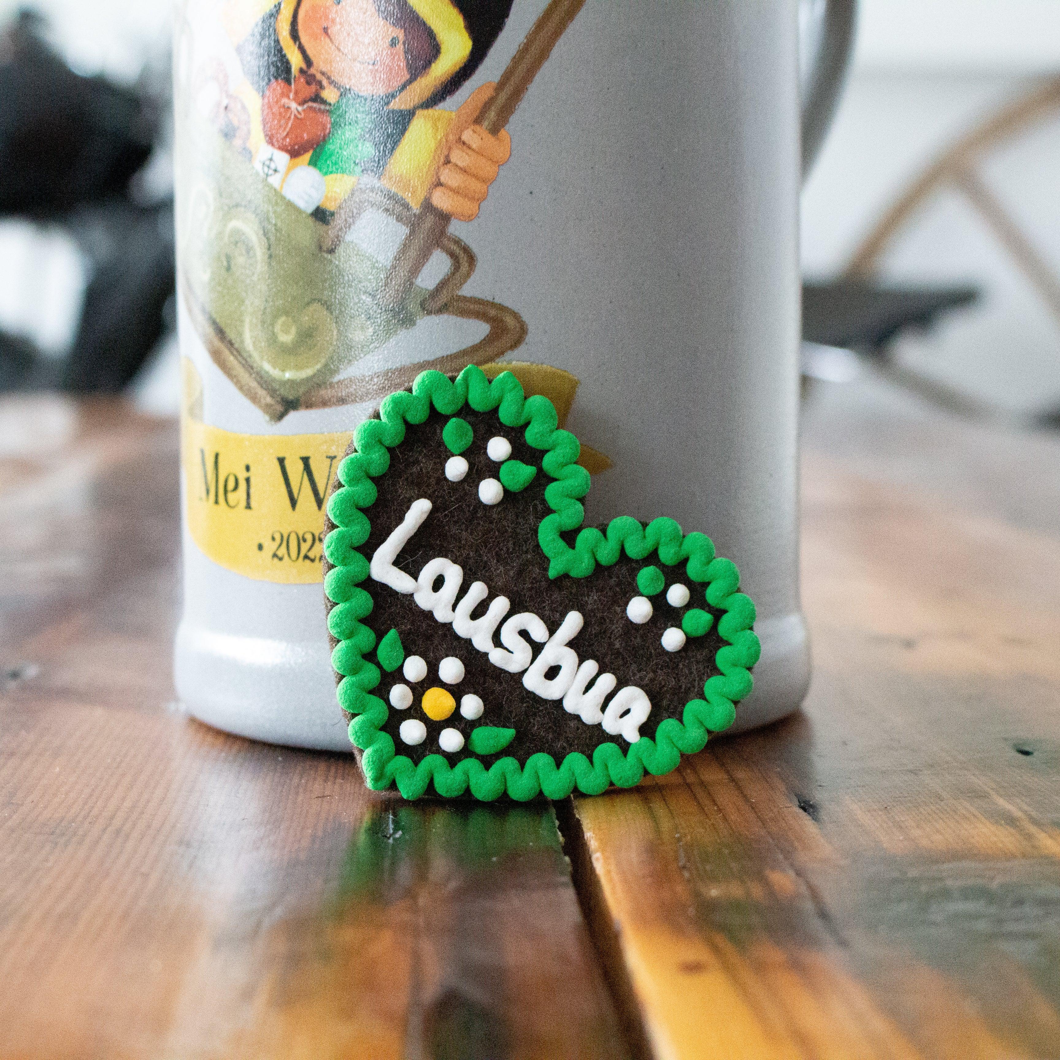 Herzförmiger Filz-Anstecker mit aufgesticktem Schriftzug „Lausbua“, Sicherheitsnadel auf der Rückseite, ca. 6,5 x 7 cm.