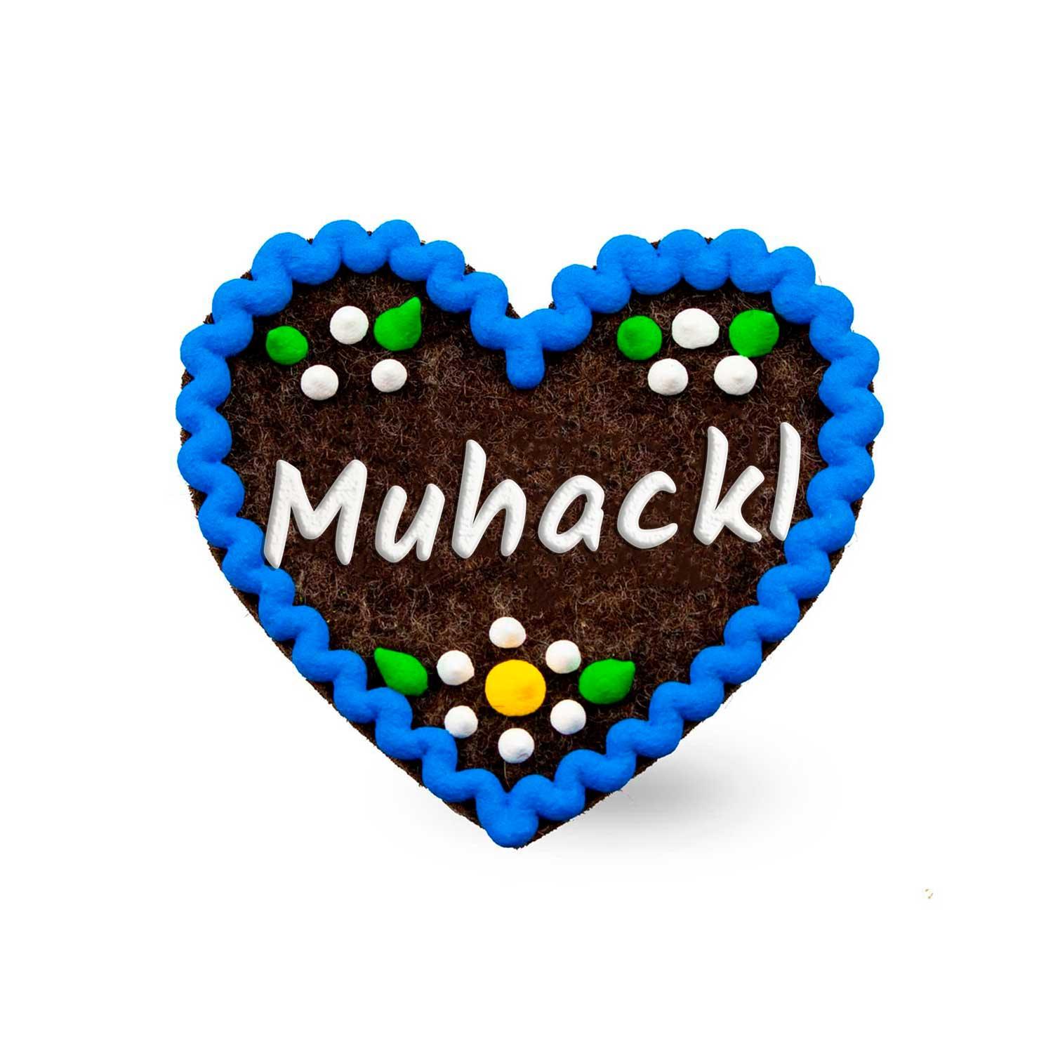 Herzförmiger Filz-Anstecker mit rundem „Muhackl“-Motiv, Sicherheitsverschluss auf Rückseite, ca. 6,5 × 7 cm.