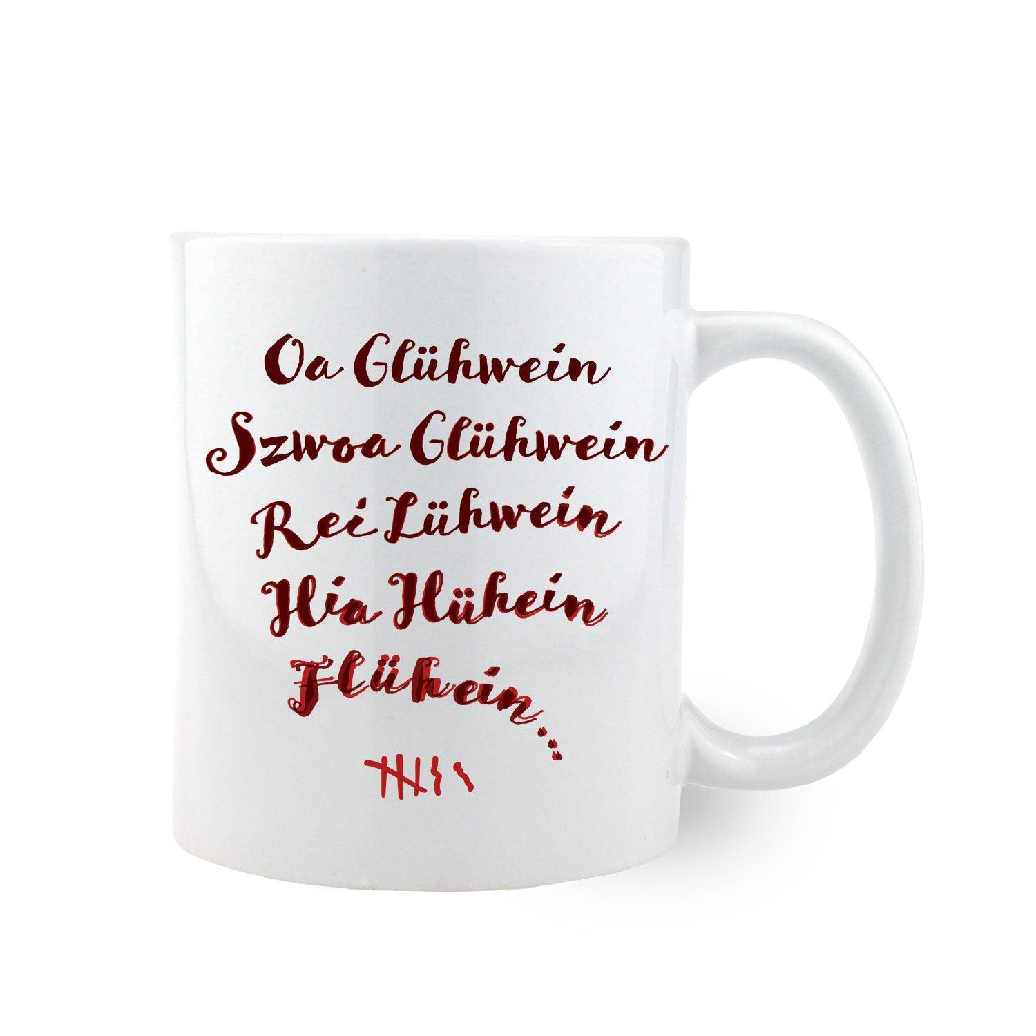 Keramiktasse in Dunkelrot mit weißem Schriftzug „Glühwein“, befüllt mit Heidelbeer-Glühwein und Glühweinbonbons.