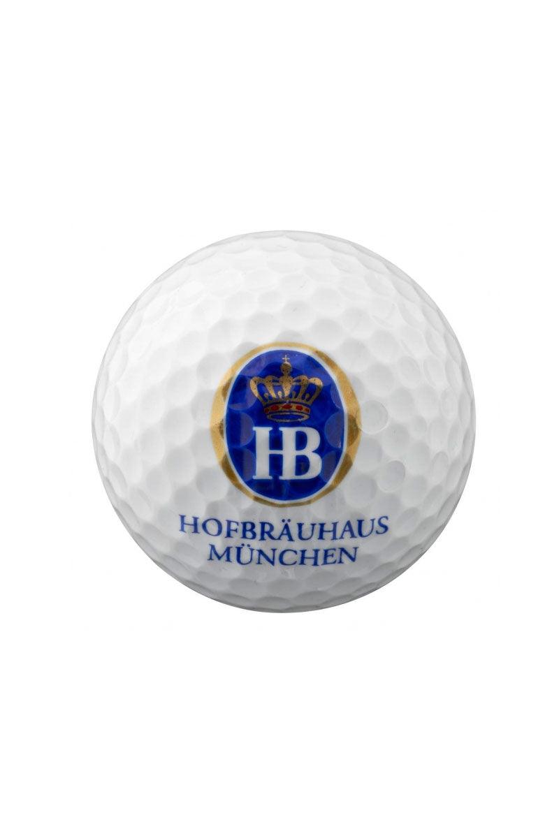 Weißer Golfball mit strukturierter Oberfläche und blauem Schriftzug „Hofbräuhaus München“ auf der Vorderseite.