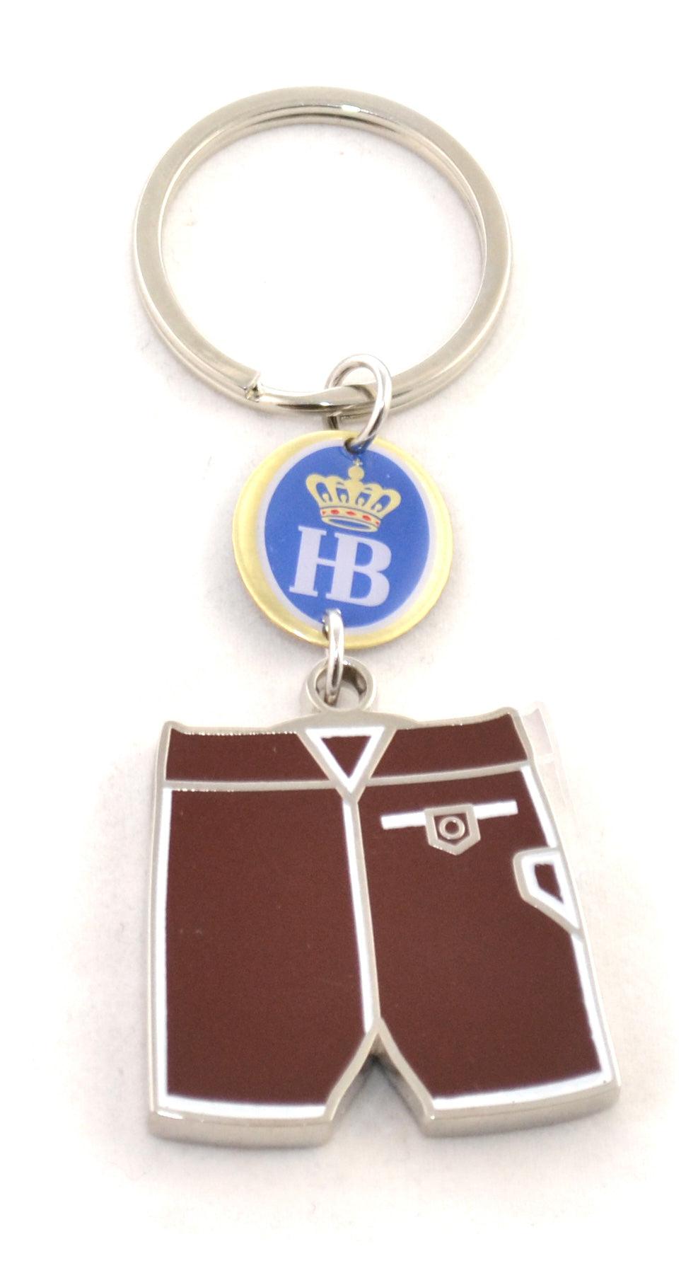 Metall-Schlüsselanhänger in Form einer braunen Lederhose mit silbernen Details und blau-weißem Wappenemblem.