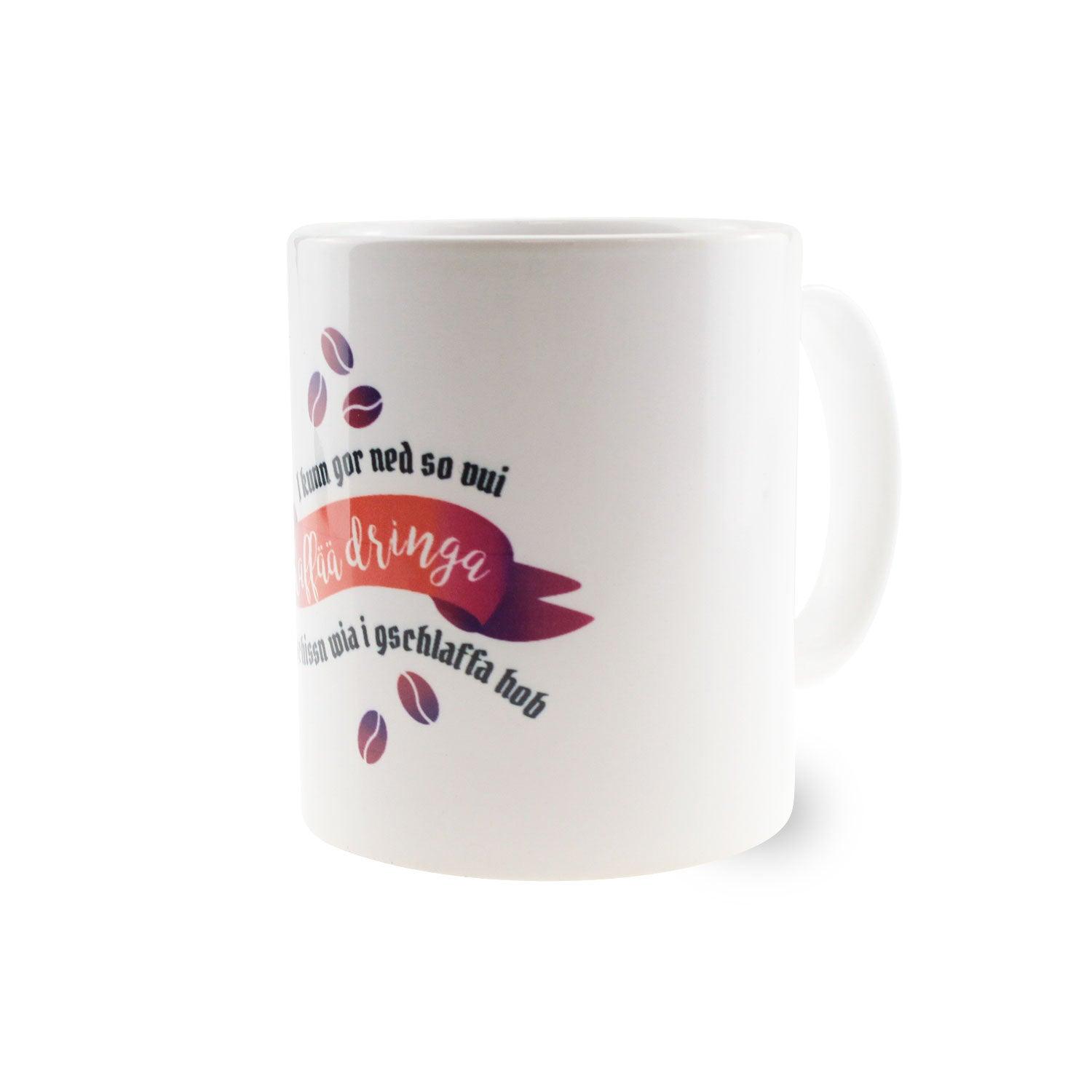Weiße Keramiktasse mit schwarzem Henkel und schwarzem Aufdruck „I kunn gor ned so vui Kaffää dringa...“, ca. 330 ml.