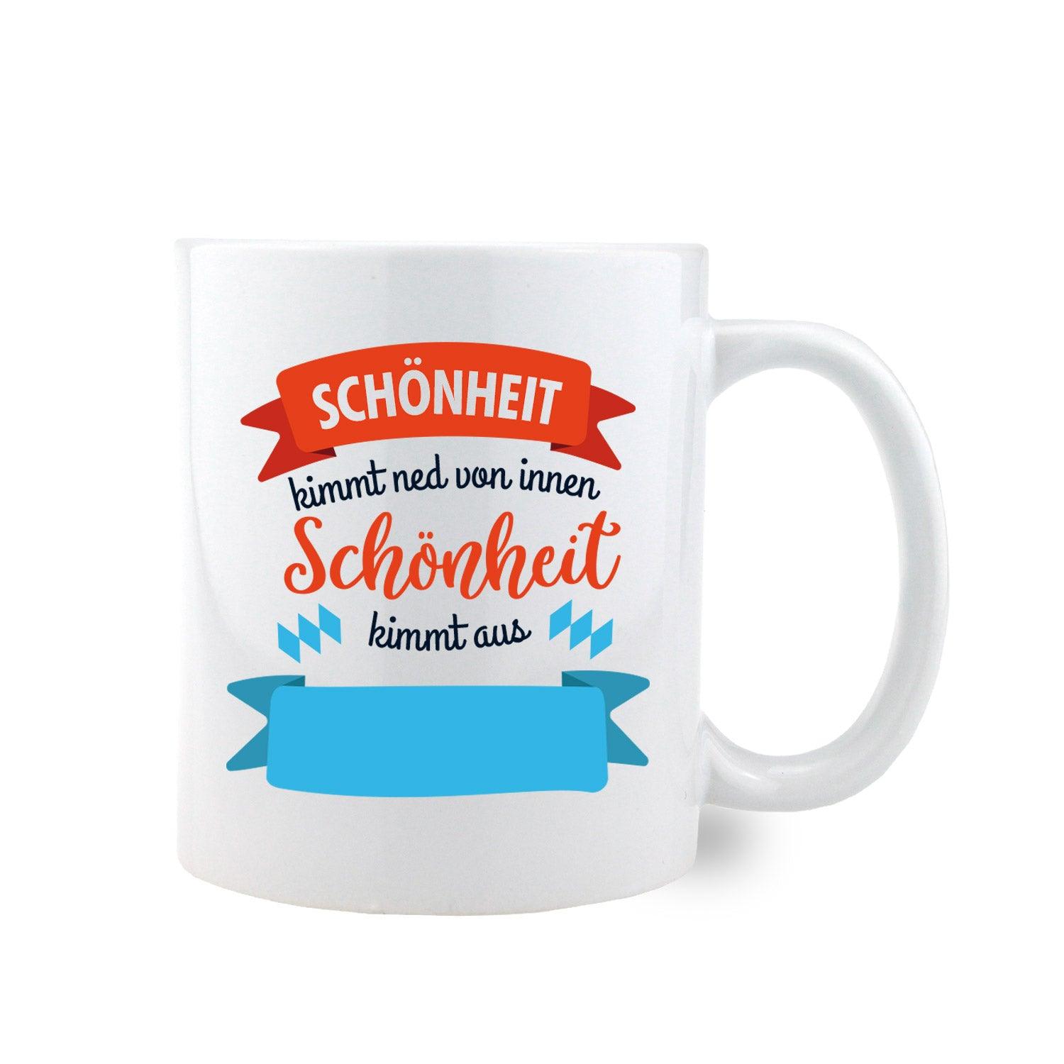 Weiße Keramiktasse mit rotem Henkel, schwarzem Schriftzug „Schönheit kimmt ned von Innen, Schönheit kimmt aus...“ und Wunschort; ca. 330 ml.