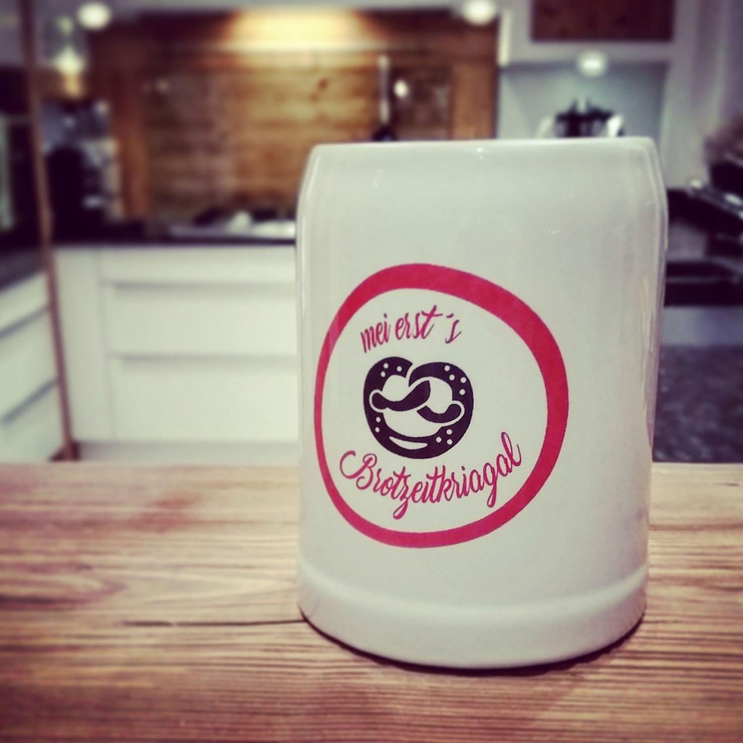 Hellgrauer Steinkrug mit Henkel, rosa Aufdruck "mei erst´s Brotzeitkriagal", runder Bauch, Inhalt 0,25 l.