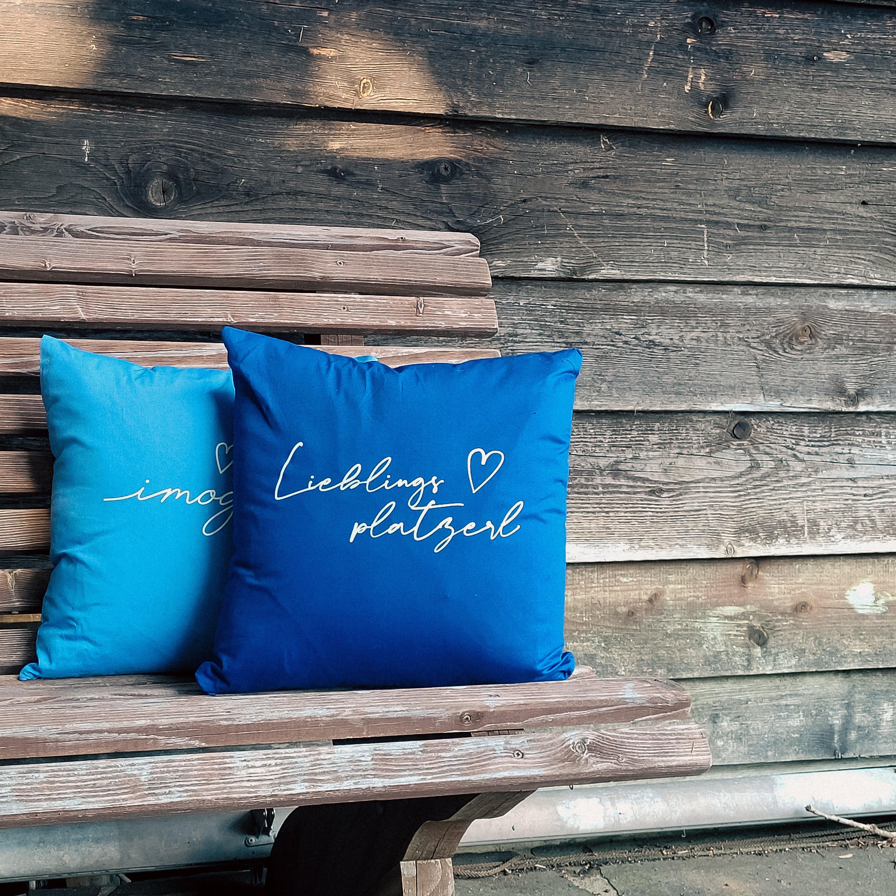 Quadratisches Dekokissen mit bayerischem Schriftzug „Lieblingsplatzerl“, sichtbare Stoffstruktur, aus Baumwolle, ca. 40 x 40 cm.