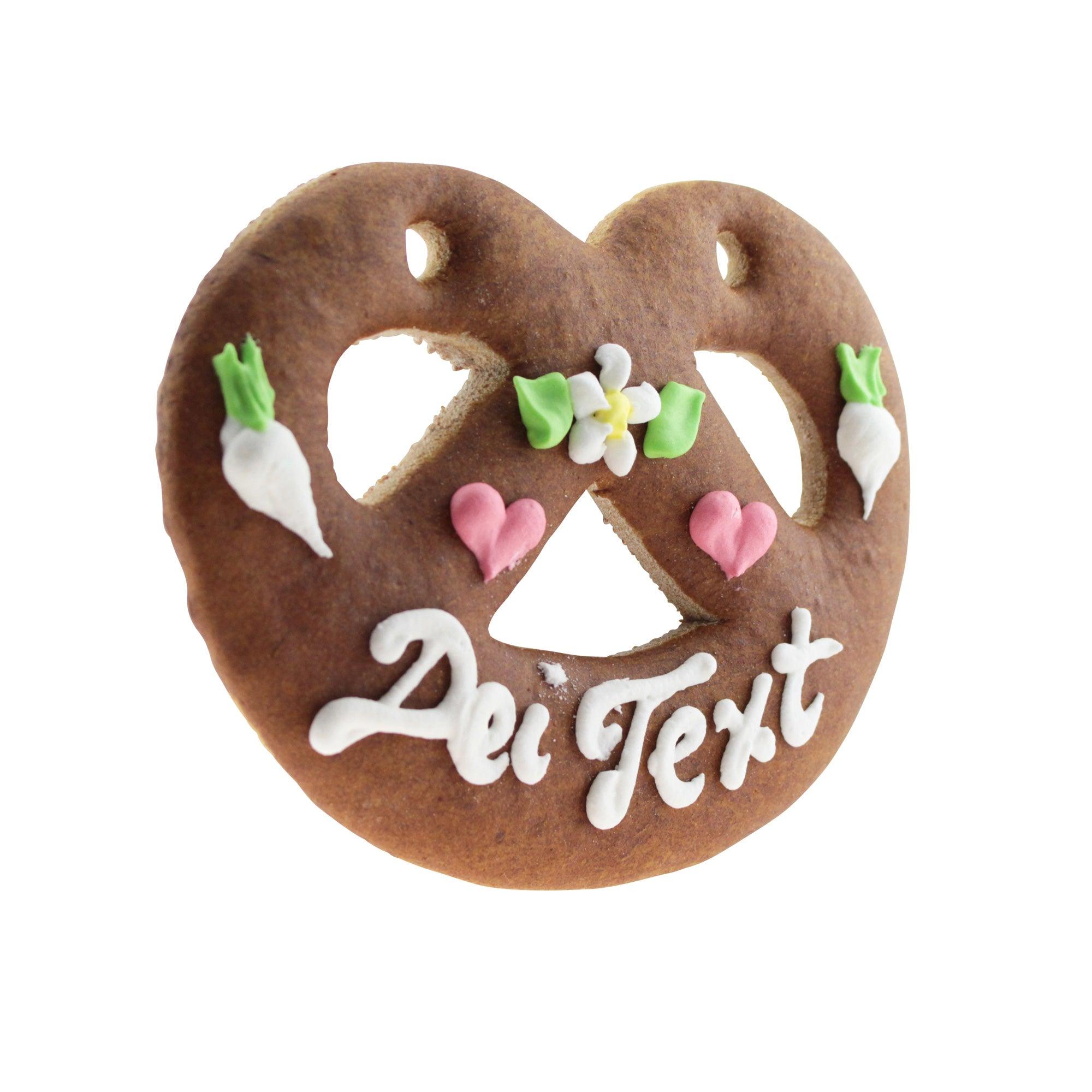 Braunes Lebkuchenherz in Brezenform mit weißer und blauer Zuckerverzierung, rotem Herz und weißem Schriftzug, ca. 12 × 15 cm.