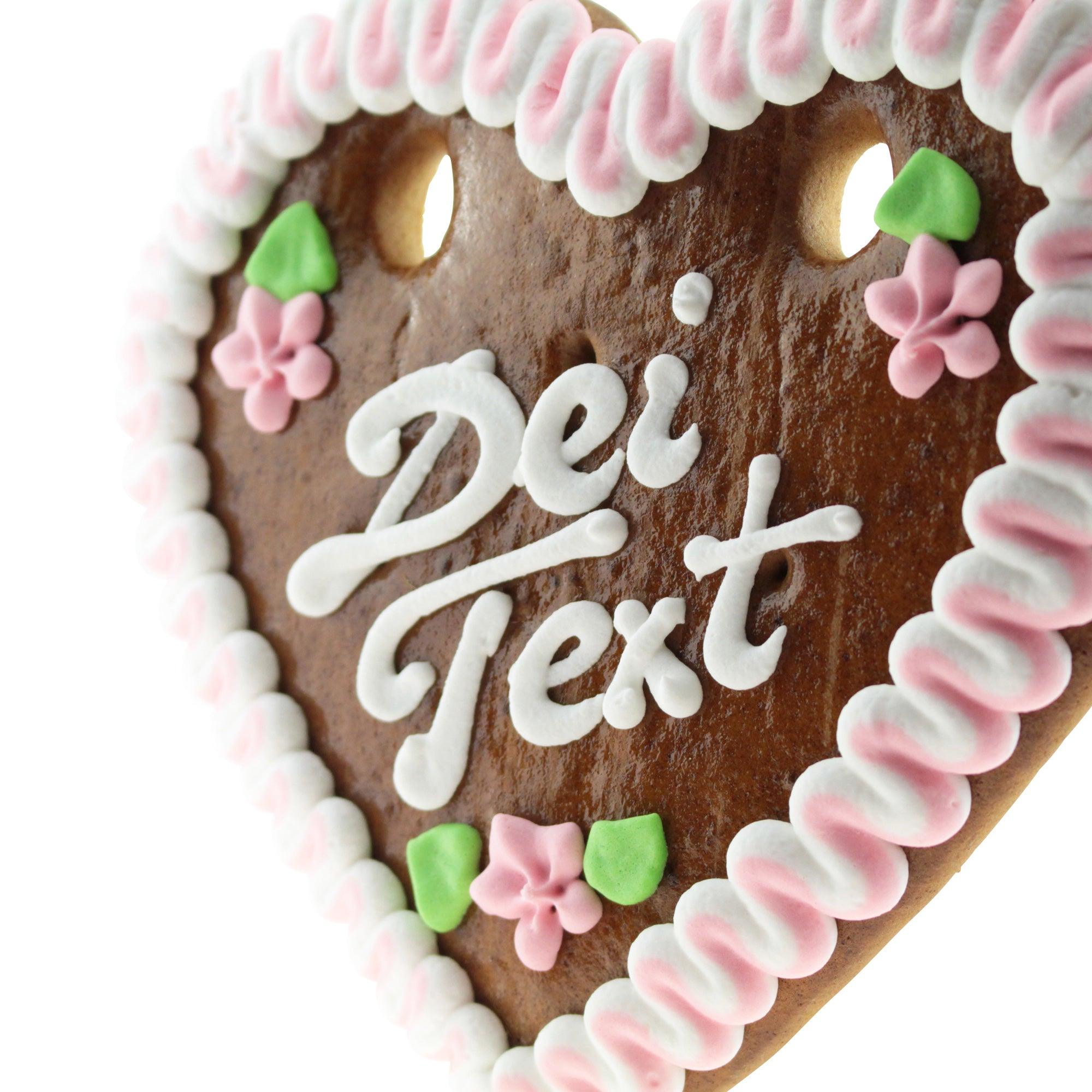 Braunes Lebkuchenherz mit weiß-blauer Zuckerverzierung und rotem Rand, zweizeiligem Wunschtext, ca. 14 × 17 cm, 100 g.