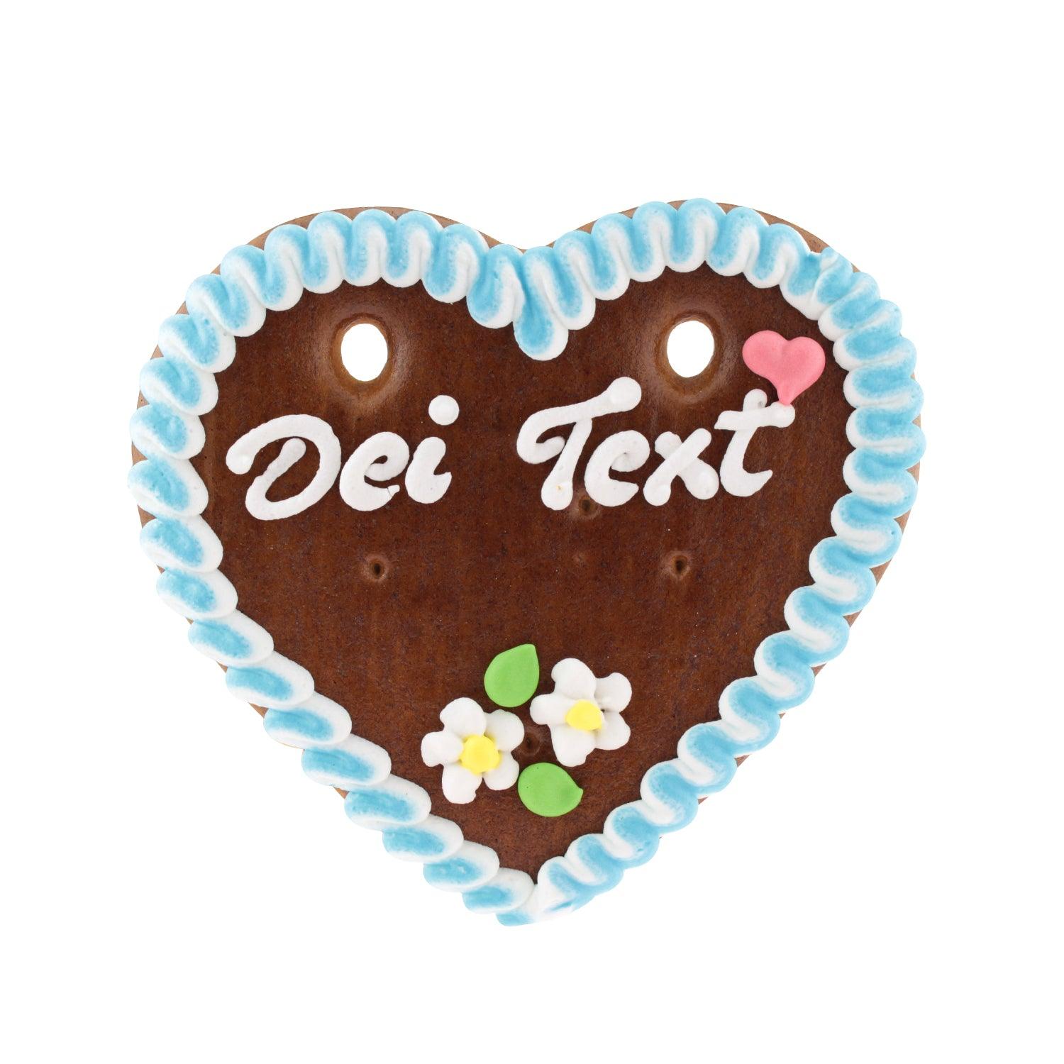 Herzförmiges Lebkuchenherz mit weißer Zuckerschrift, rosa Rand und Blumenmotiv, personalisierbar, ca. 14 x 17 cm.