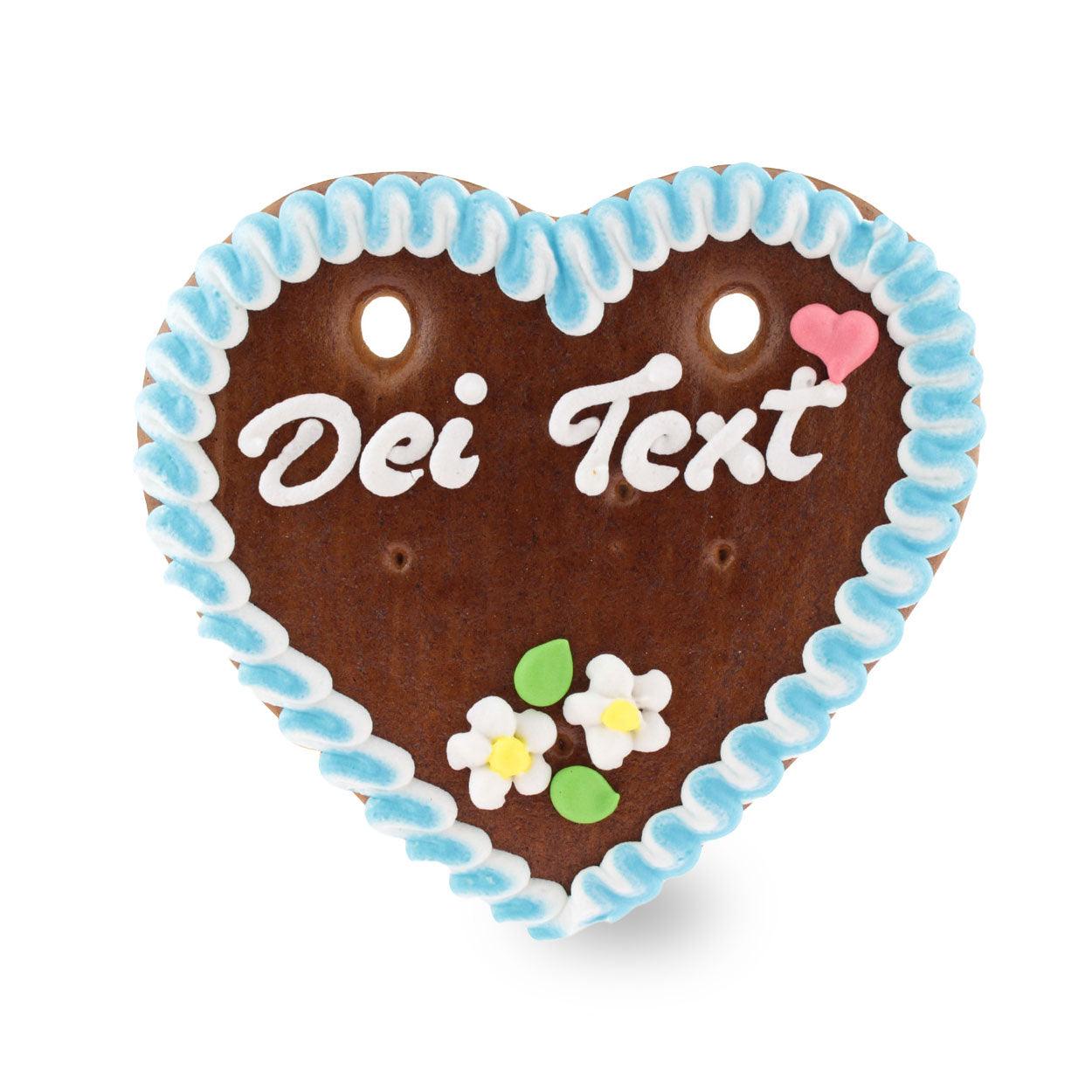 Herzförmiges Lebkuchenherz mit weiß-rotem Zuckerrand, blau-weißem Blumenmotiv und individualisierbarem Schriftzug; handgefertigt aus braunem Lebkuchen, ca. 22 x 23 cm, 180 g.