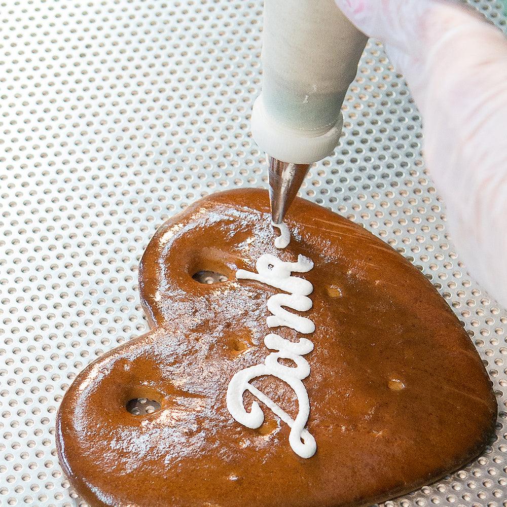 Herzförmiges Lebkuchenherz mit weiß-blauer Zuckerglasur, roten Rosen, Wunschtext und Randverzierung; ca. 22 x 23 cm, 180 g.