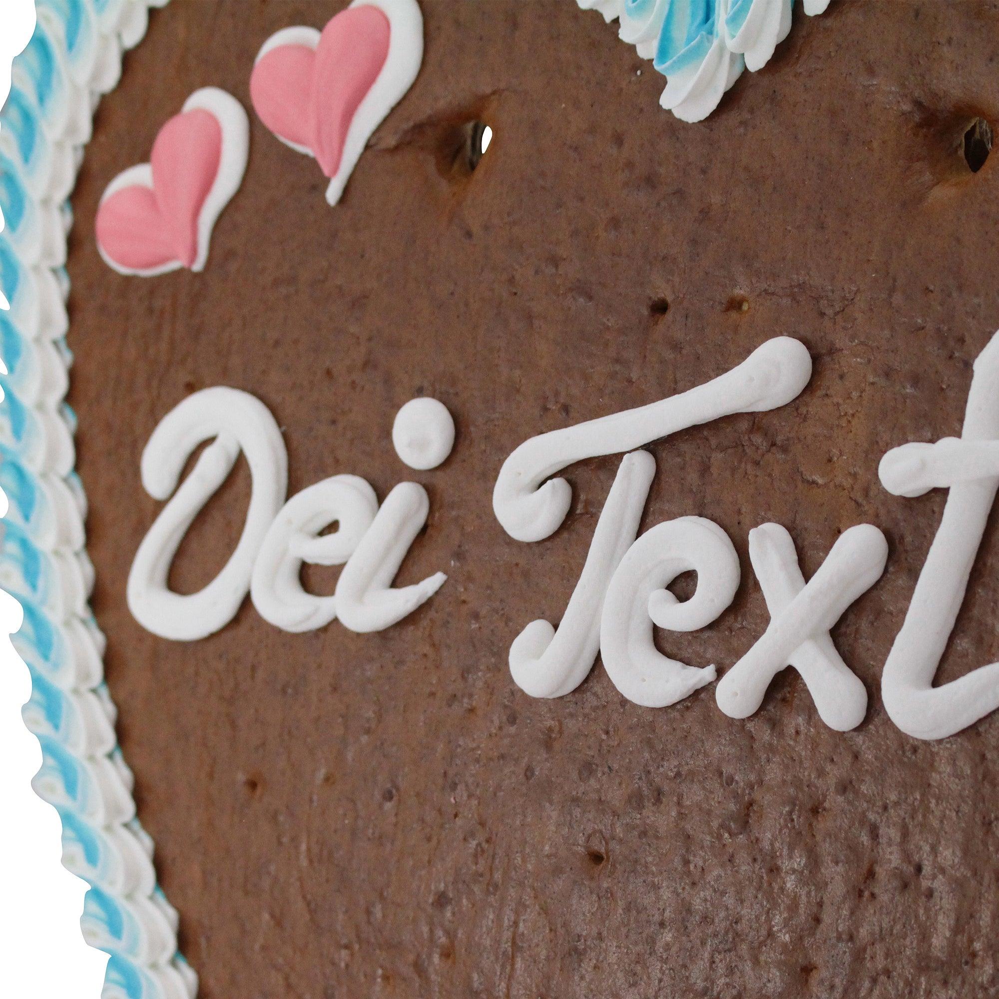 Großes herzförmiges Lebkuchen mit rosafarbenem Rand, Blumenmuster und individuellem Text auf braunem Zuckerguss; ca. 50 × 48 cm, 1 kg.