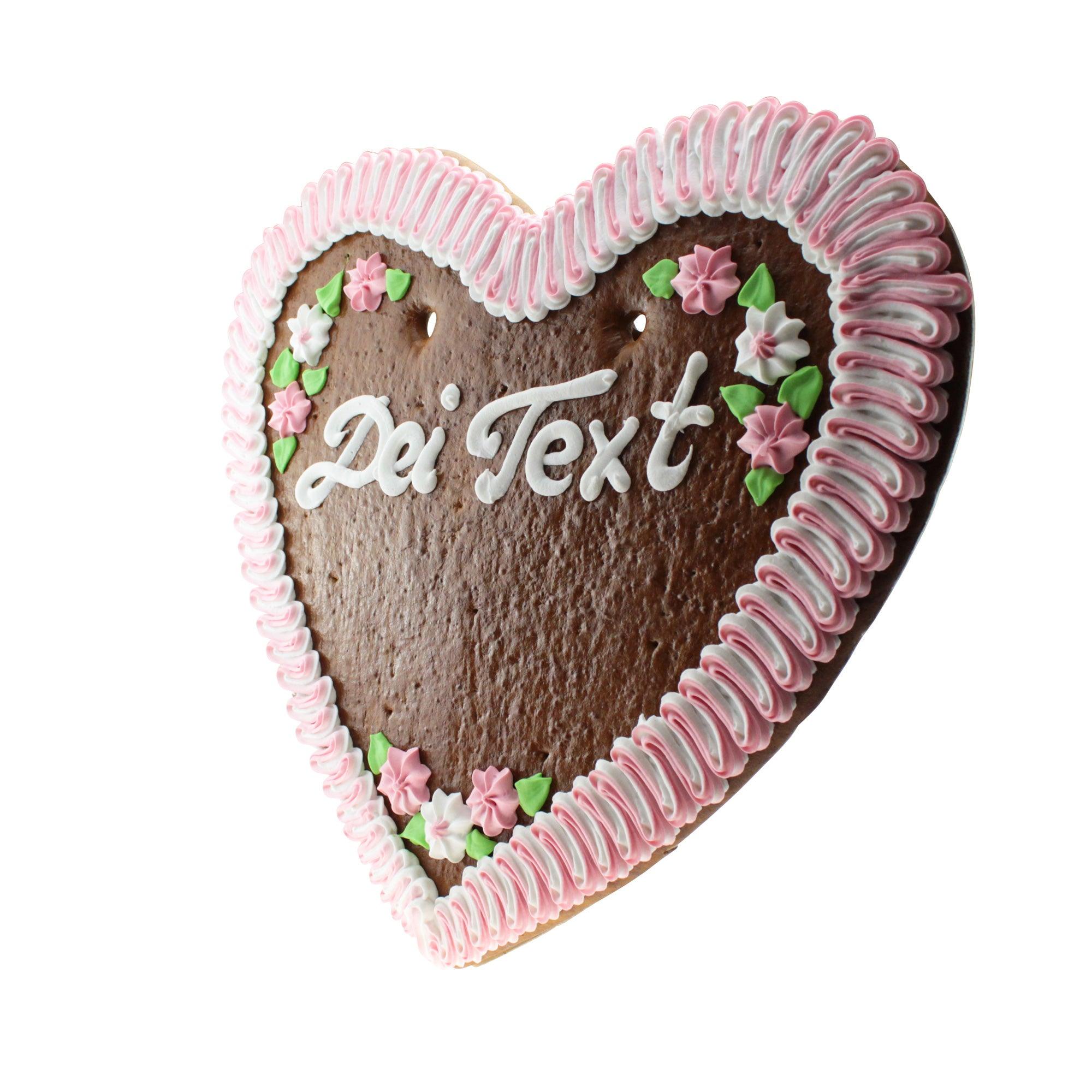 Großes, herzförmiges Lebkuchenherz mit weißer Zuckerverzierung und individuellem Schriftzug auf braunem Teig, rosa Rand, ca. 50 x 48 cm.