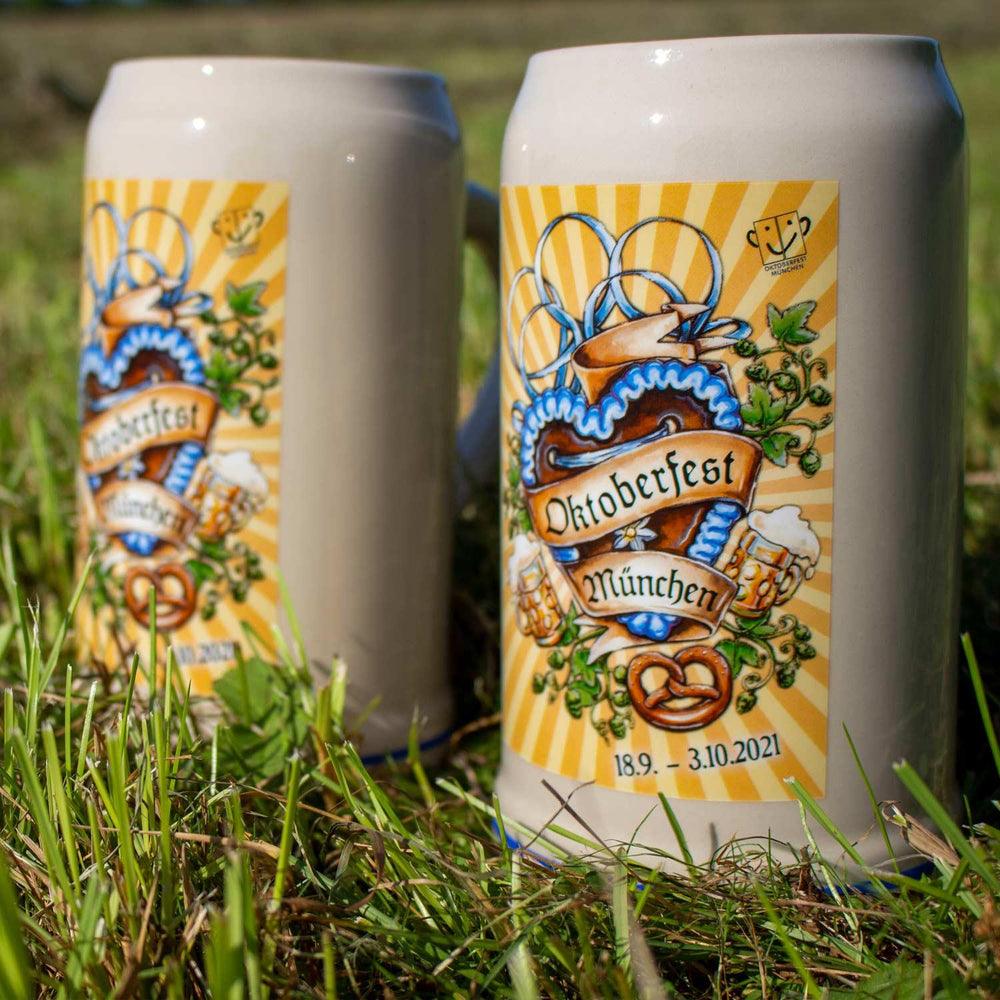 Oktoberfestkrug aus grauem Steingut mit farbigem Plakatmotiv 2021 und blauem Schriftzug, zylindrisch geformt.