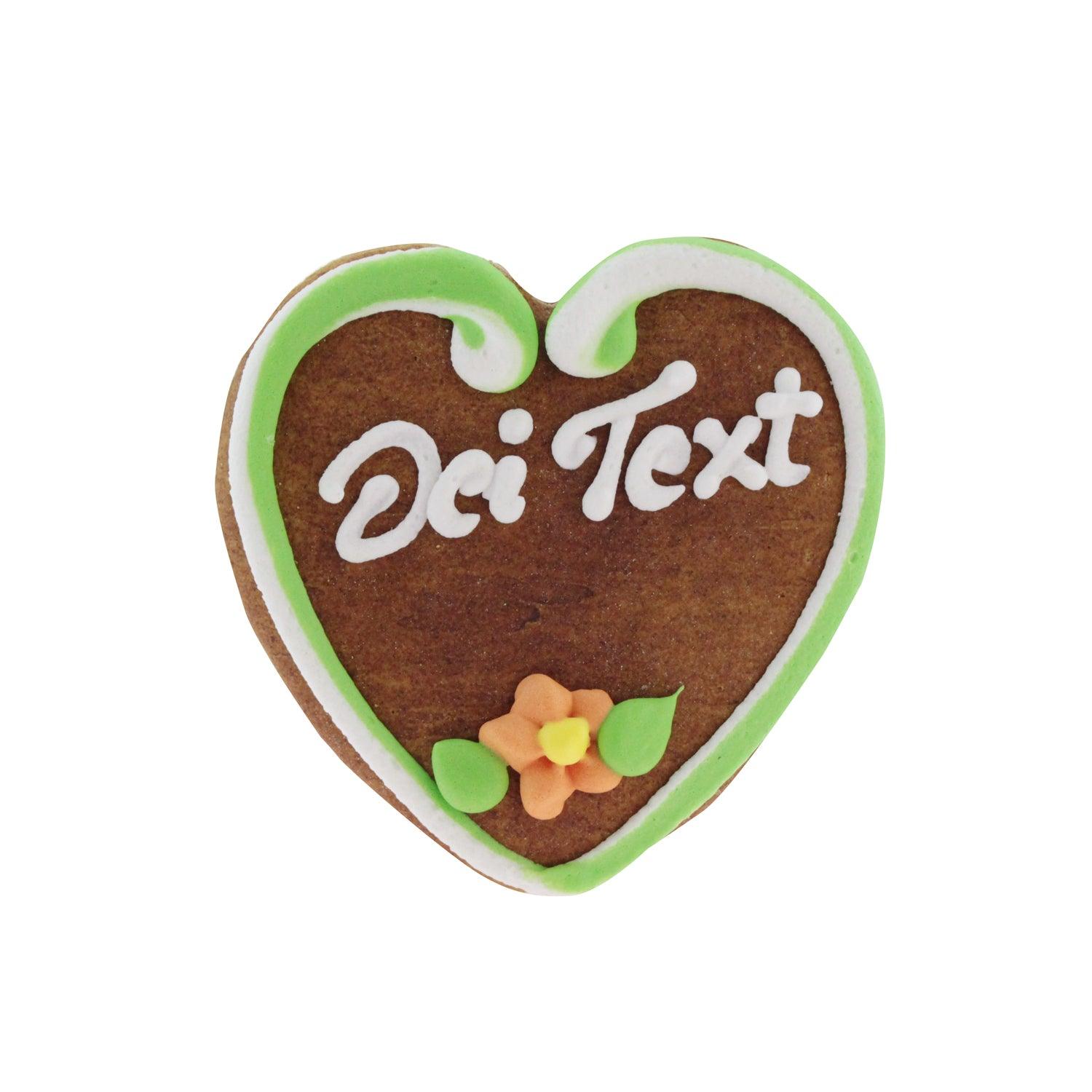 Herzförmiges Lebkuchenherz mit weißer Zuckerschrift und rosa Rand, handdekoriert, braune Oberfläche, ca. 10 x 10 cm.