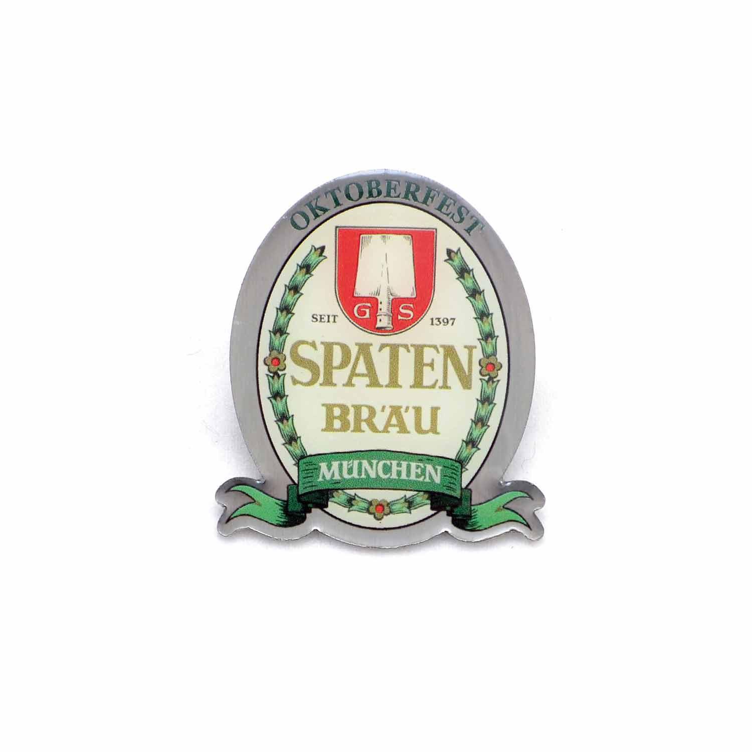 Goldfarbener Pin in Wappenform mit rotem Spaten-Logo und weißem Schriftzug „Spaten Bräu“, ca. 30 × 40 mm.