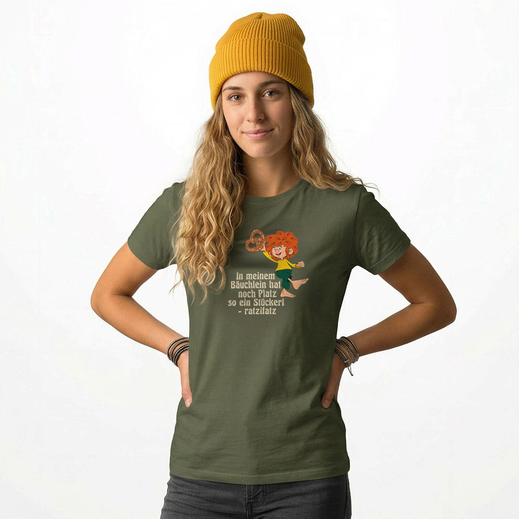 Junge Frau im olivgrünen Pumuckl Damen T-Shirt mit rotem Haare Kobold und Brezel-Motiv, dazu lockige Haare und gelbe Mütze.