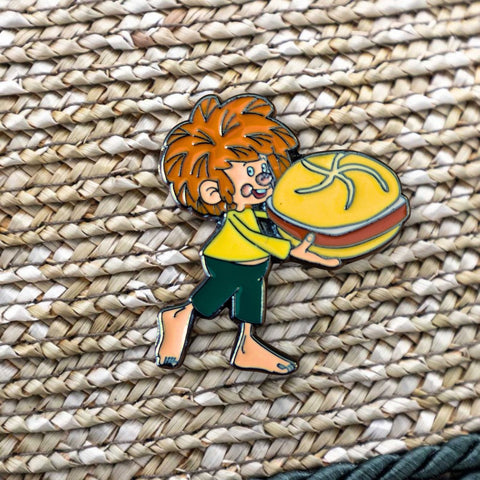 Pumuckl Pin Leberkassemmel – Emaille Anstecker: Pumuckl trägt eine Leberkassemmel im Arm, auf Strohgeflecht