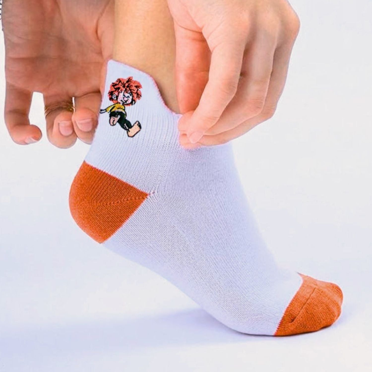 Weiße Pumuckl Sneaker Socken mit orangefarbenem Fersen- und Zehenbereich, und einem gestickten Pumuckl Motiv.