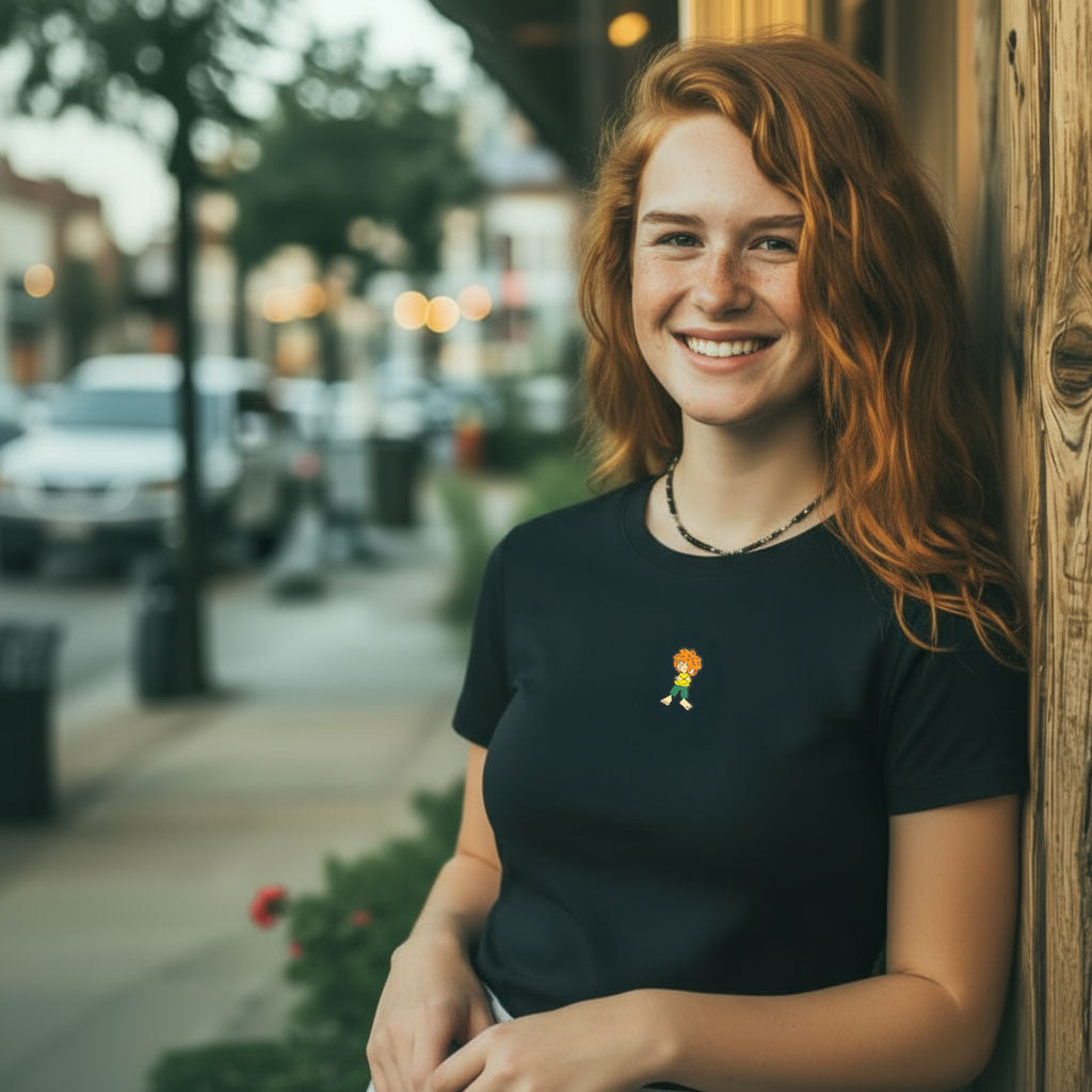 Lachende Frau mit rotem Haar trägt schwarzes ®Pumuckl Damen T-Shirt "Grantla" mit Pumuckl-Motiv am Straßenrand.
