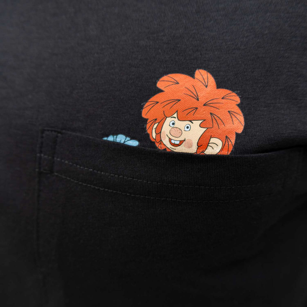 Schwarzes T-Shirt mit lachendem Pumuckl, der neugierig aus der Brusttasche schaut, verspieltes Schabernack Design.
