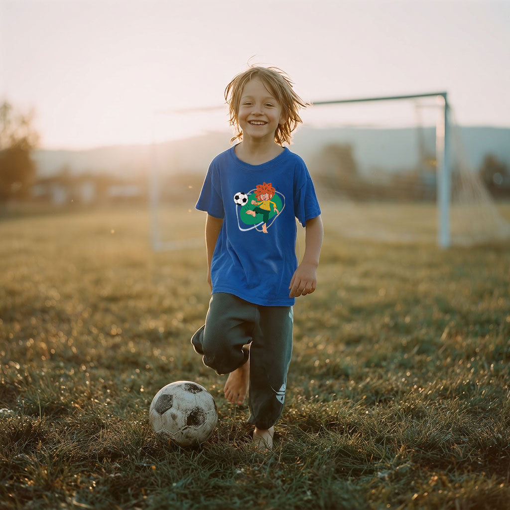 Glückliches Kind im blauen Pumuckl Fußball T-Shirt auf einem Fußballfeld bei Sonnenuntergang.